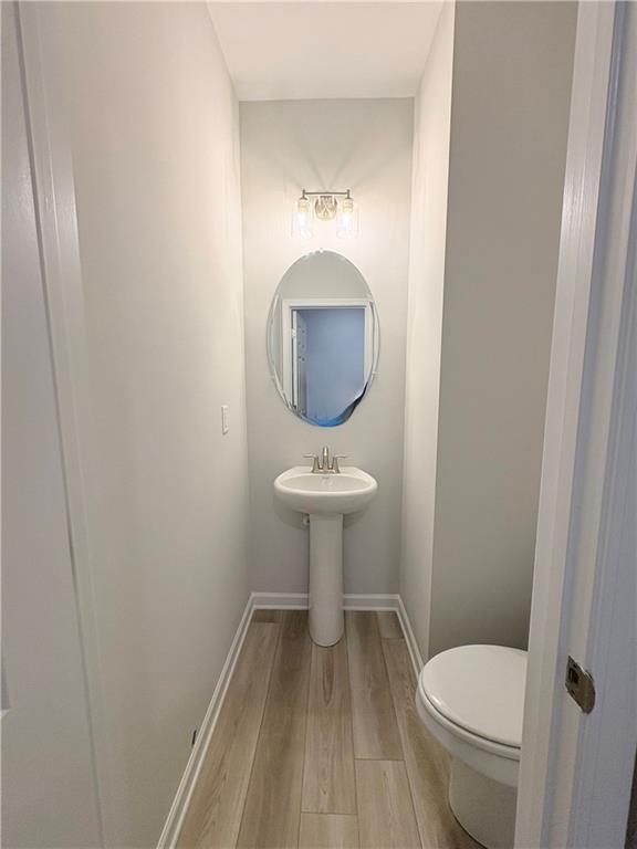 Compact powder room with pedestal sink, round mirror, and luxury vinyl plank flooring in Davidson Homes The Wake E, Cumming, GA