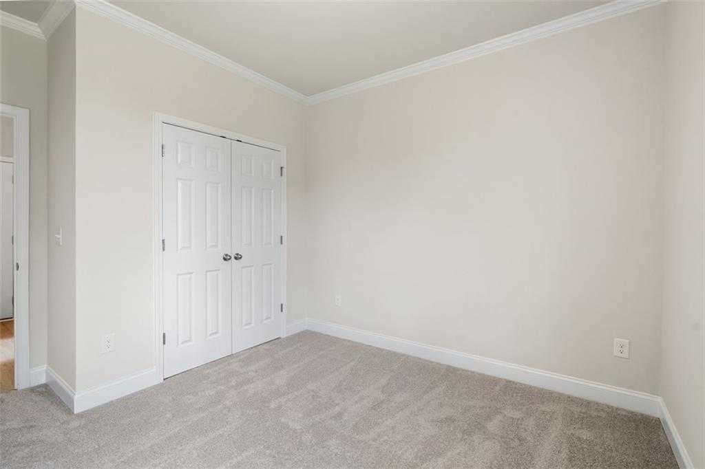 Spacious empty bedroom with white double closet doors, beige walls, and carpeted floor in Davidson Homes The Willow D at Wehunt Meadows, Hoschton