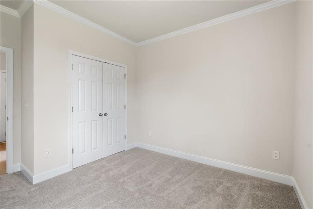 Spacious empty bedroom with white double closet doors, beige walls, and carpeted floor in Davidson Homes The Willow D at Wehunt Meadows, Hoschton