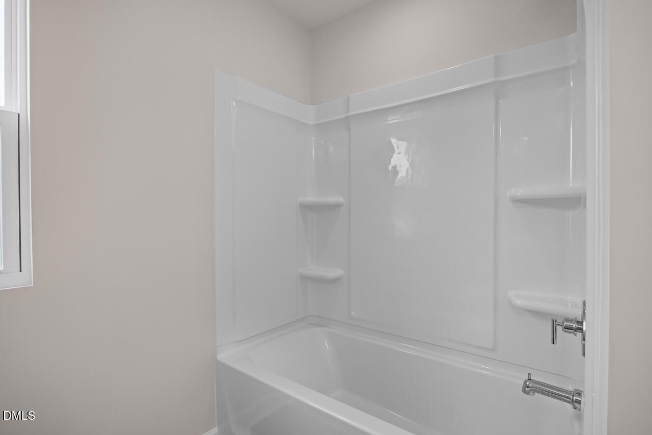 White tub and shower combination with built-in shelving in a bathroom at The Willow B in Woodland Crossing, Zebulon, NC.