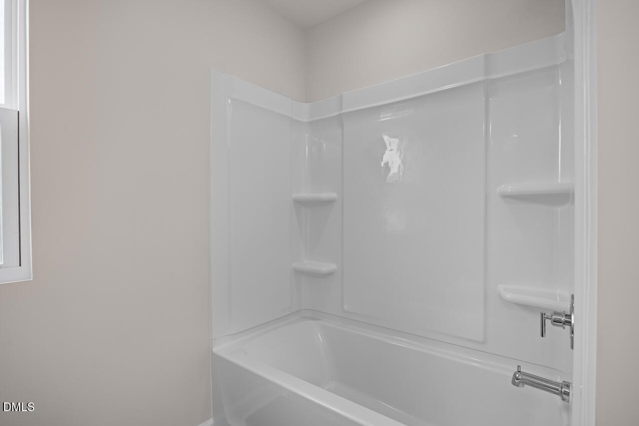 White tub and shower combination with built-in shelving in a bathroom at The Willow B in Woodland Crossing, Zebulon, NC.