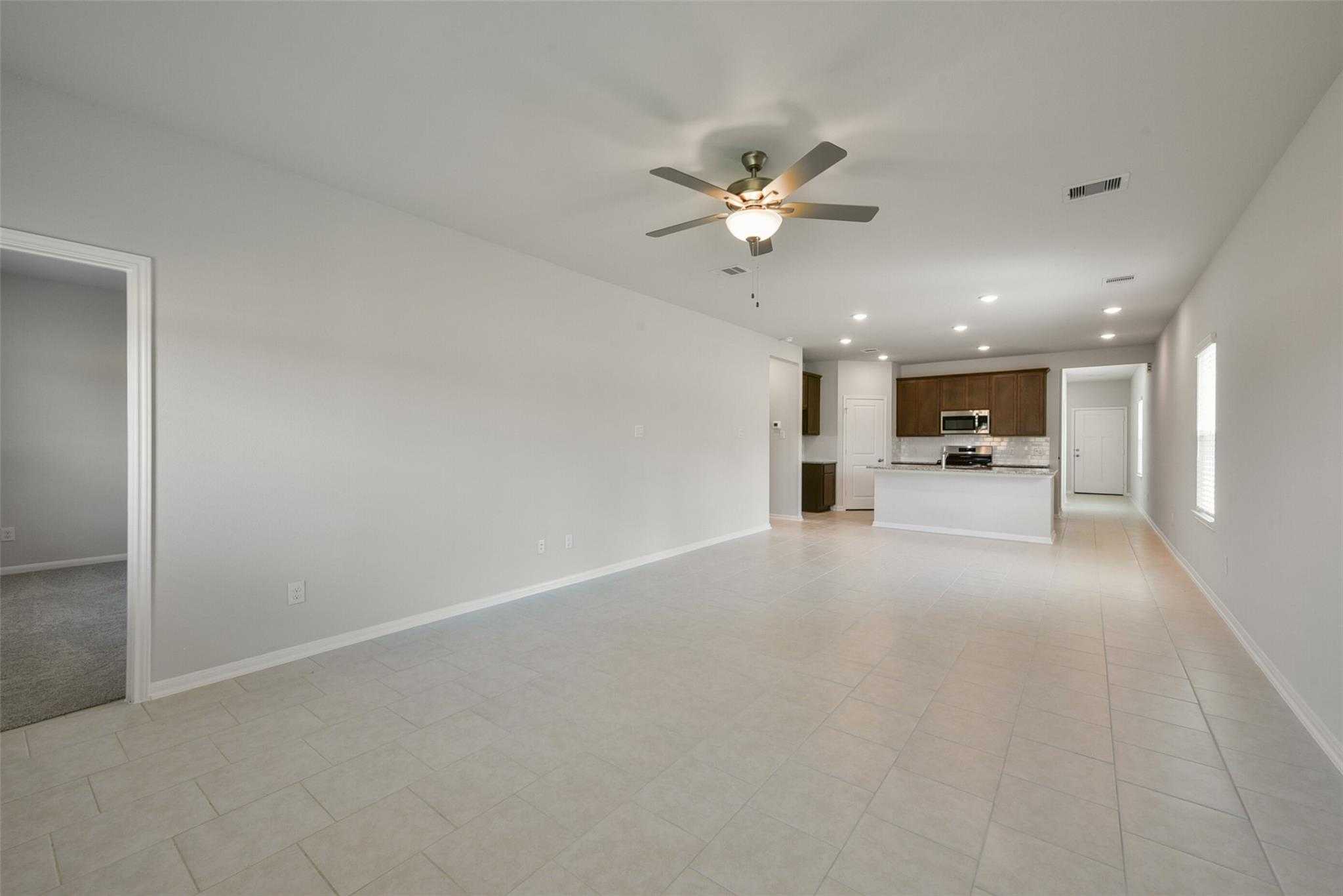 Spacious open living room with kitchen island, ceiling fans, white cabinets, and tile floors in Davidson Homes Sabine E, Dayton, Texas