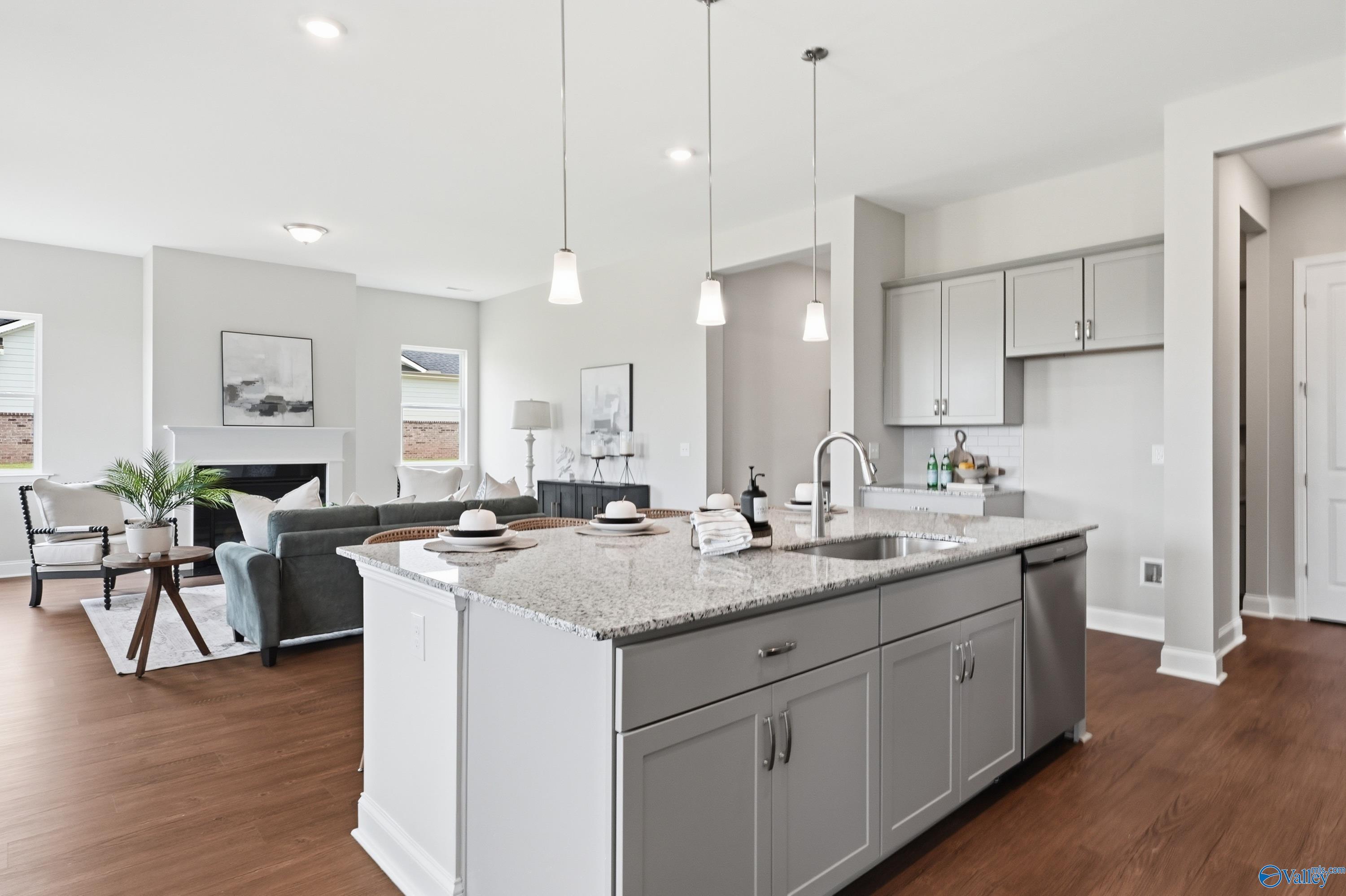 Open-concept kitchen with granite island, gray cabinets, and pendant lights adjoining living room with fireplace in Davidson Homes Arcadia B, Huntsville AL