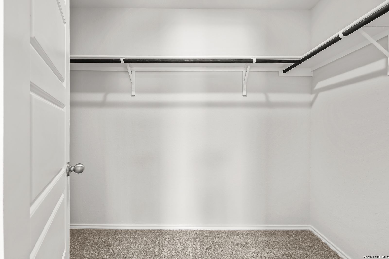 Walk-in closet with white shelving and neutral carpeting in The Gillian B floor plan at Meadows at Oak Creek, San Antonio.