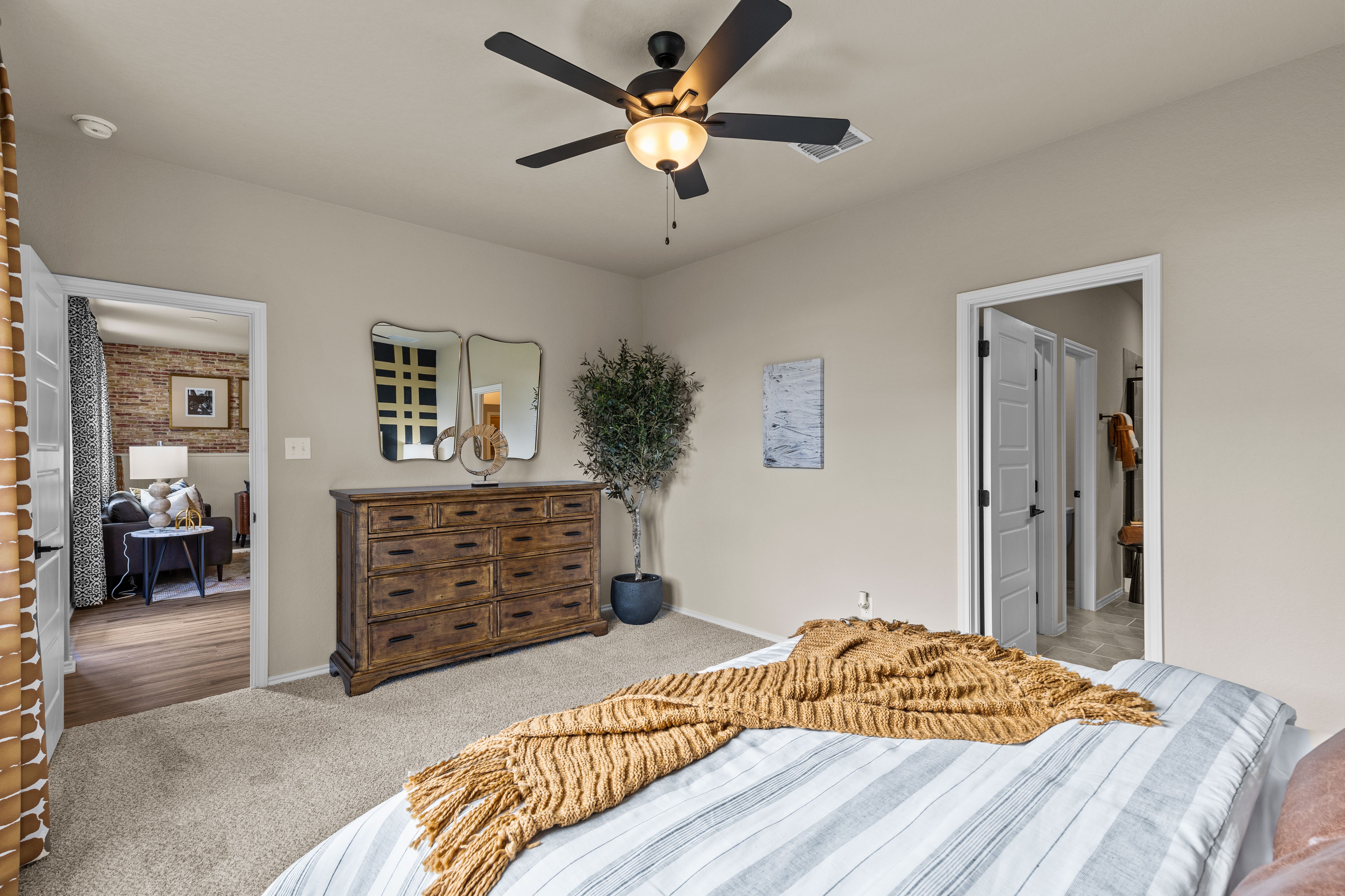 Cozy bedroom interior at Morgan Meadows in San Antonio TX with striped bed, wooden dresser, potted plant, and ceiling fan