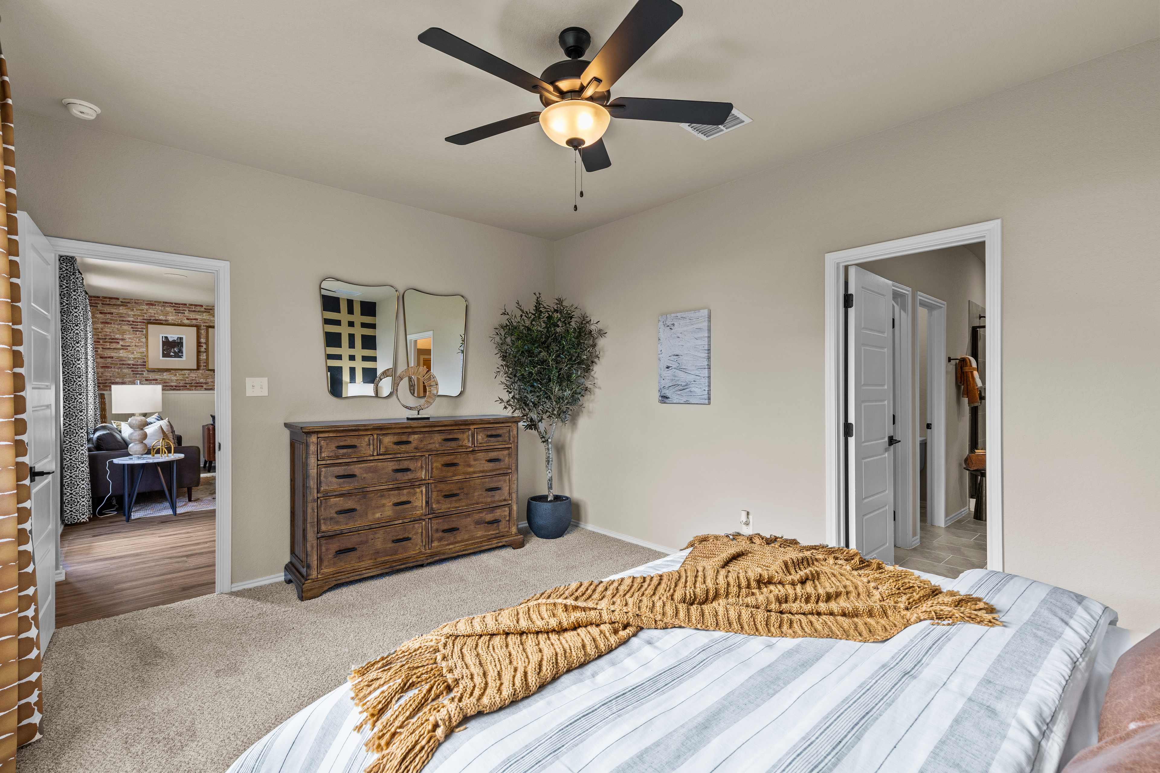 Cozy bedroom interior at Morgan Meadows in San Antonio TX with striped bed, wooden dresser, potted plant, and ceiling fan