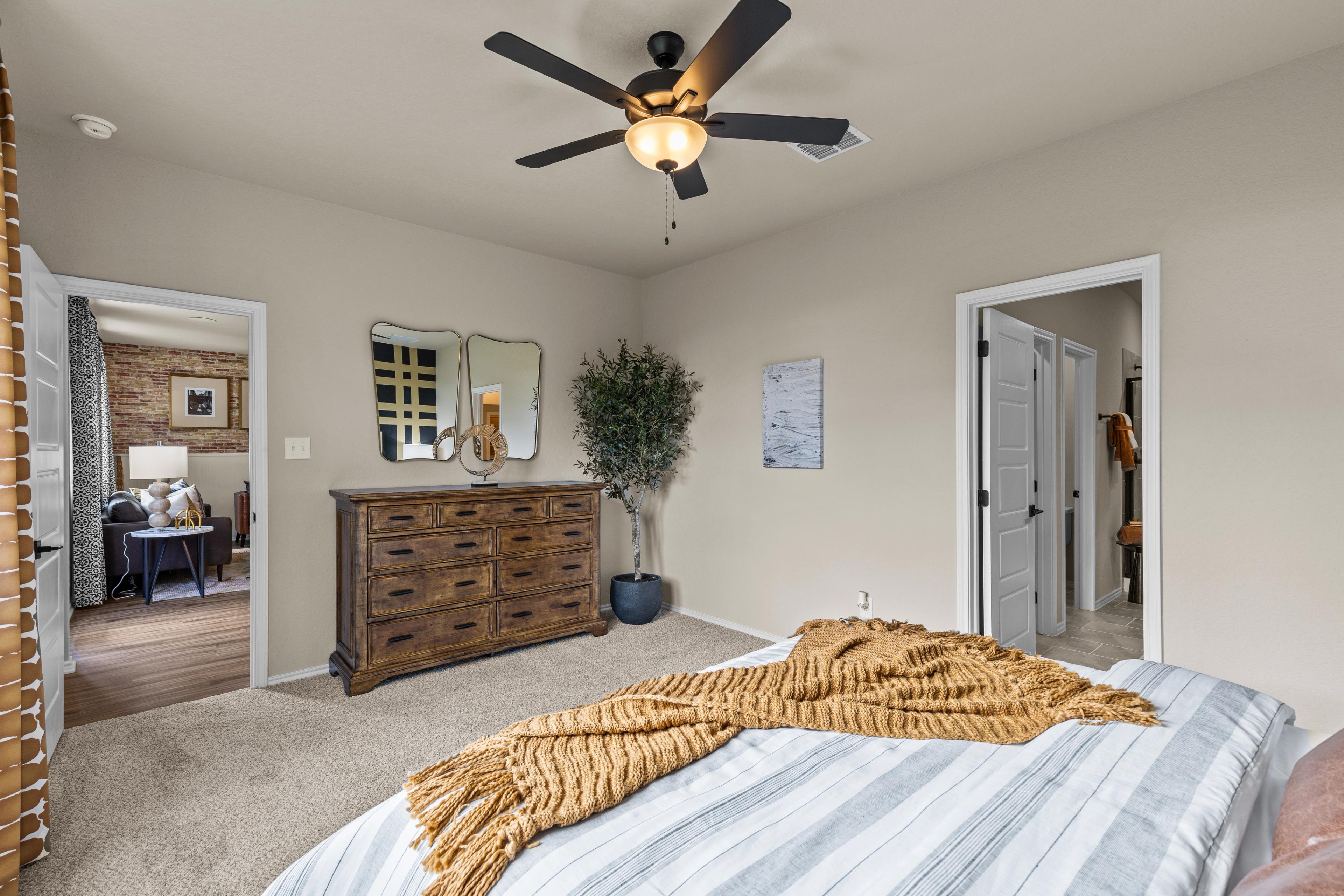 Cozy bedroom interior at Morgan Meadows in San Antonio TX with striped bed, wooden dresser, potted plant, and ceiling fan