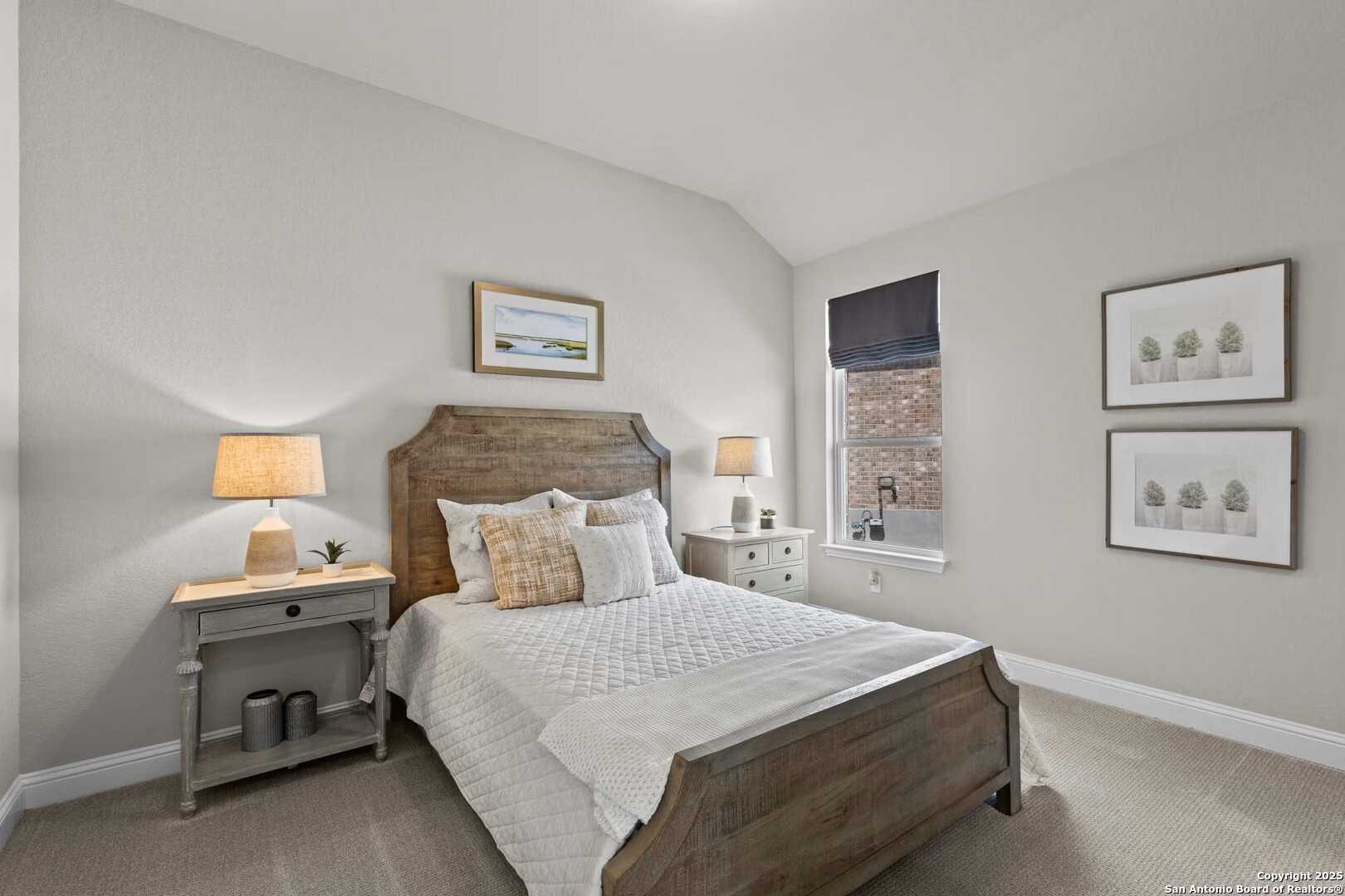 Cozy secondary bedroom with wooden bed frame, white bedding, orange pillows, gray walls, and framed art in Davidson Homes The Garner A, Castroville, Texas