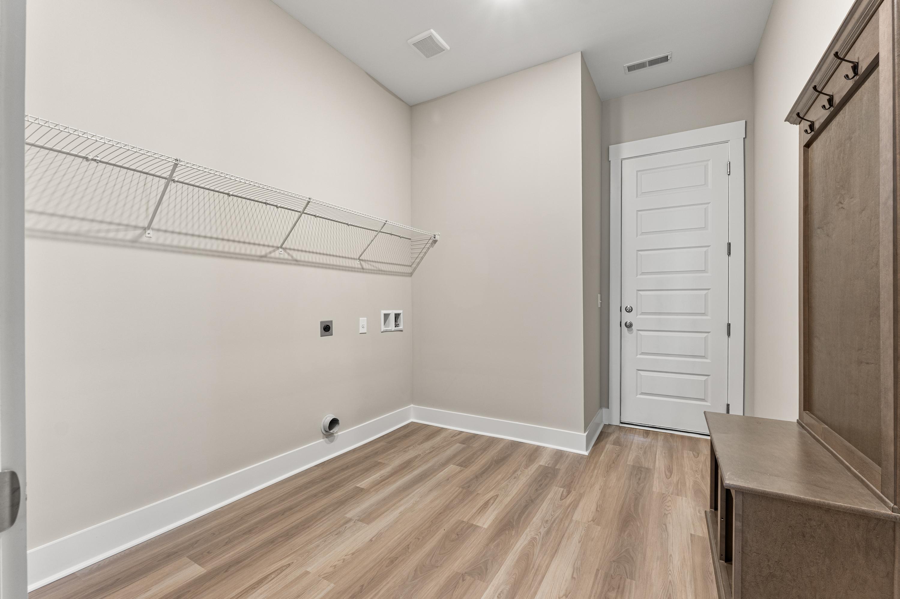 Spacious laundry room in The Oxford C with wire shelving, washer-dryer hookups, built-in wooden bench, and neutral beige walls