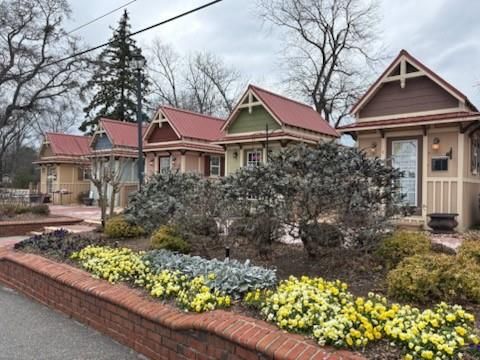 Row of colorful Craftsman cottages with red roofs, yellow flower beds, and brick paths in Cedar Farms, Winder, Georgia