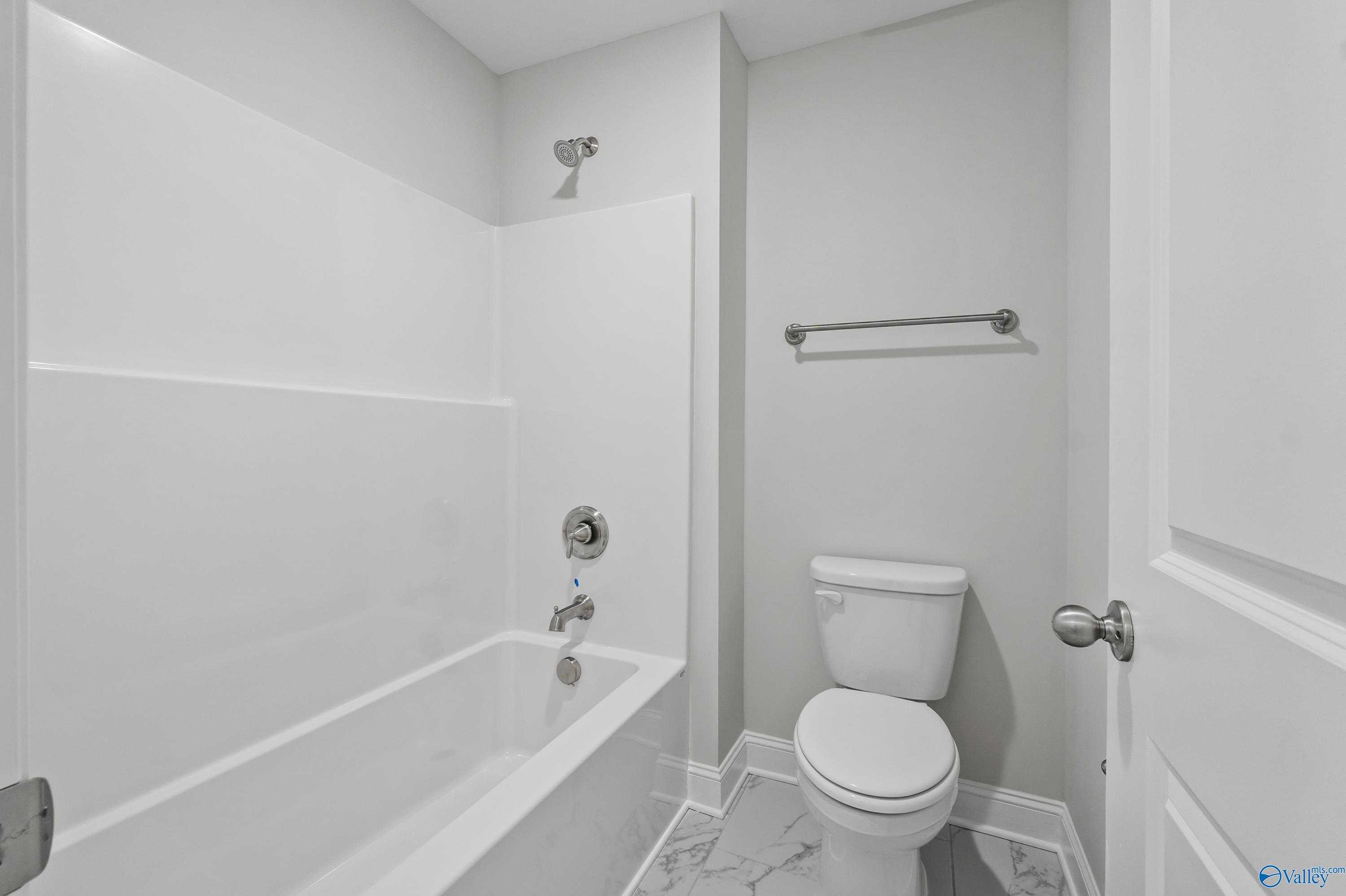 Modern white bathroom with tiled tub-shower combo, toilet, and neutral walls in Davidson Homes The Camden, Huntsville AL