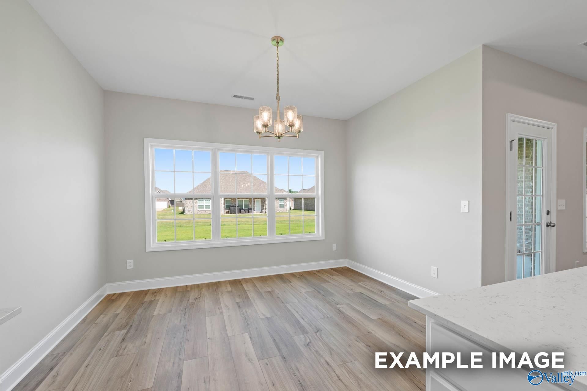 Bright dining nook with chandelier, hardwood floors, and large windows overlooking lush backyard in Davidson Homes Montgomery B, Hartselle AL
