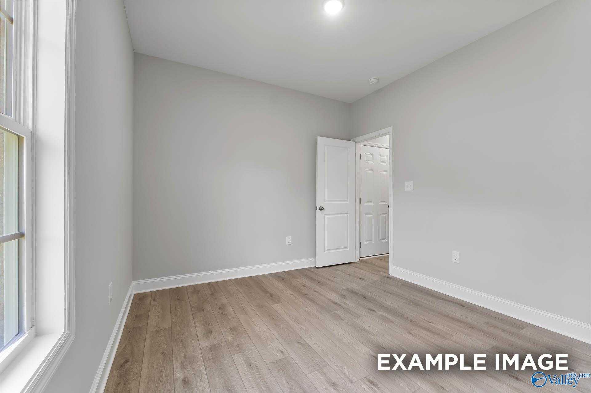 Bright secondary bedroom with light gray walls, large window, and light wood floors in Davidson Homes The Daphne C, New Market, Alabama