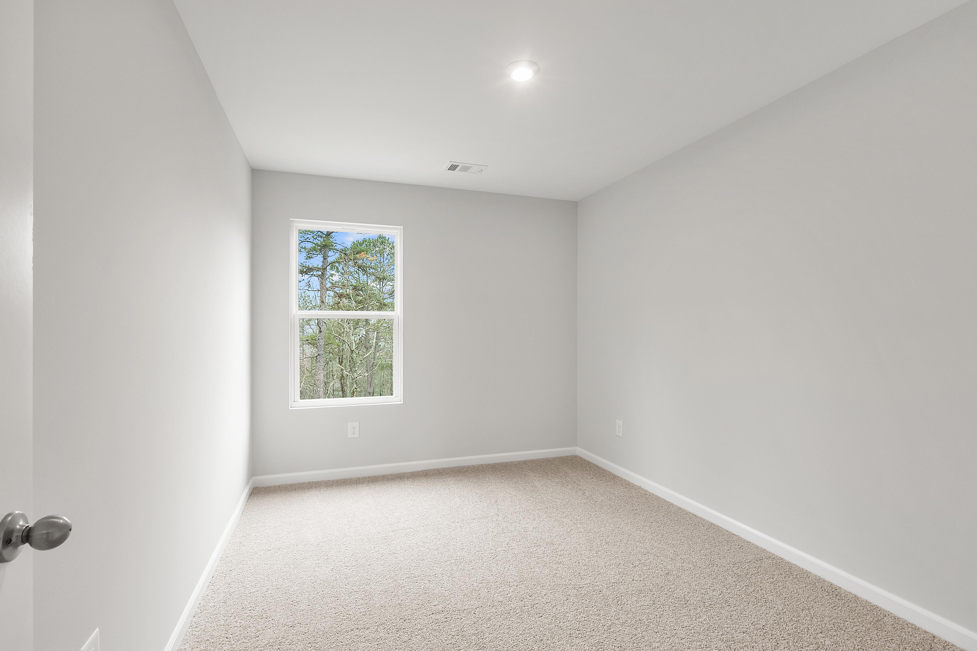 Upper floor bedroom in The Durant A with light gray walls, neutral carpet, and double window overlooking pine trees