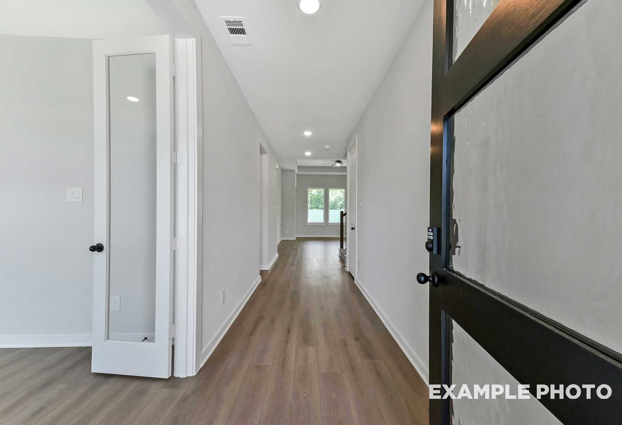 Spacious hallway in The Sequoia home with light wood floors, French doors, white walls, and bedroom entries