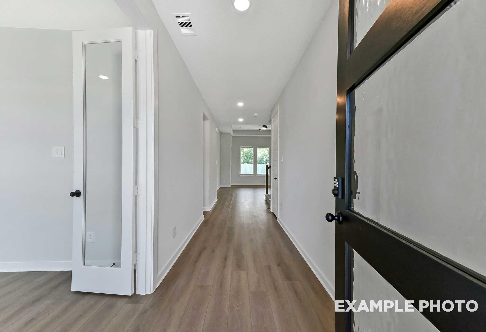 Spacious hallway in The Sequoia home with light wood floors, French doors, white walls, and bedroom entries