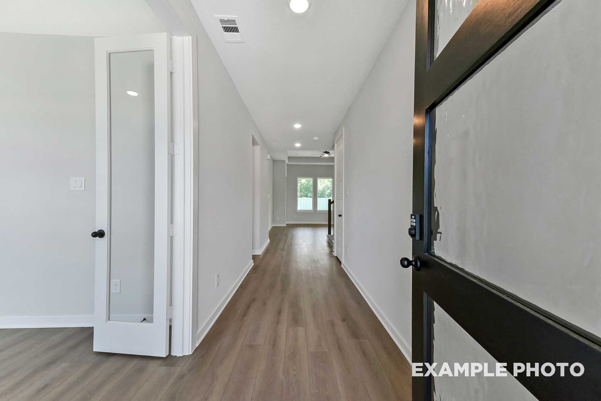 Spacious hallway in The Sequoia home with light wood floors, French doors, white walls, and bedroom entries
