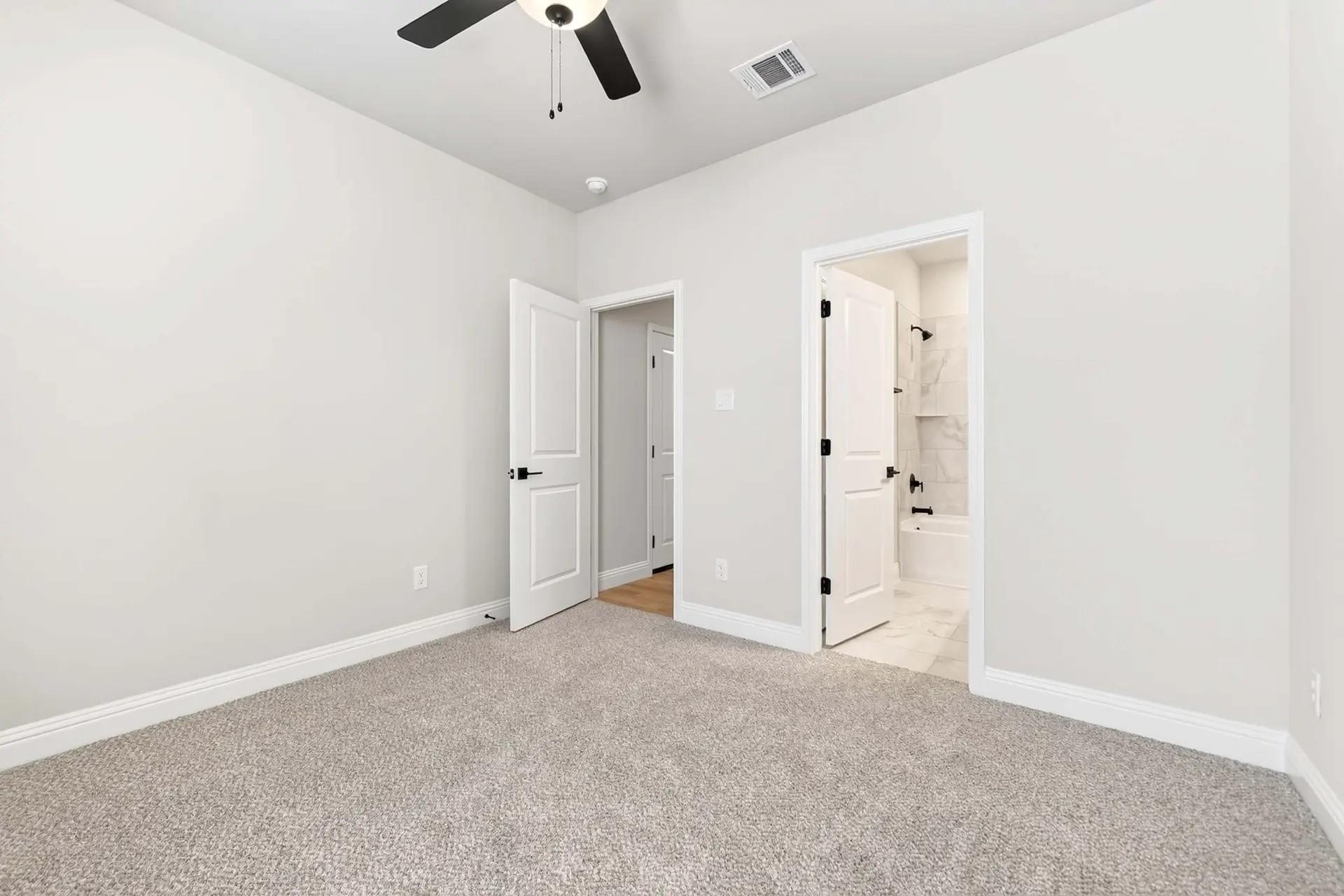 Spacious bedroom with plush carpet and ensuite bathroom in The Holly C floor plan by Davidson Homes in Heartland, Texas.