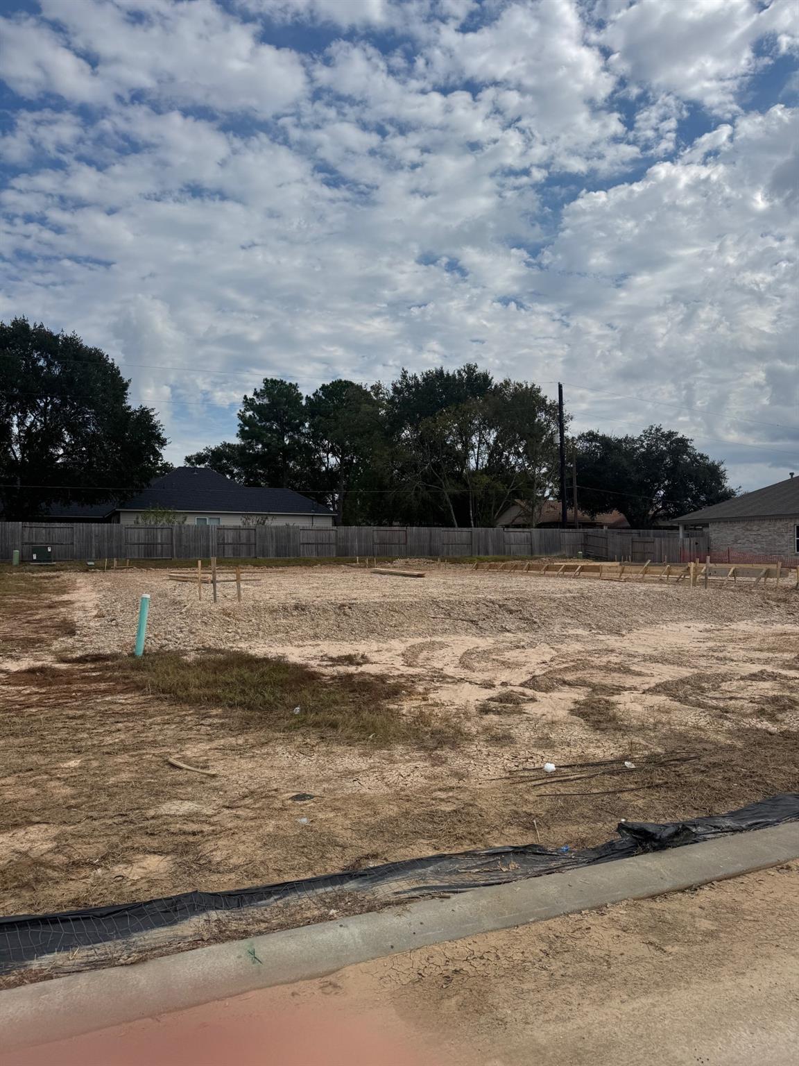 Cleared lot with wooden fencing, green stakes, and dirt ground for Davidson Homes Blanco E in Windmill Estates, Magnolia, Texas