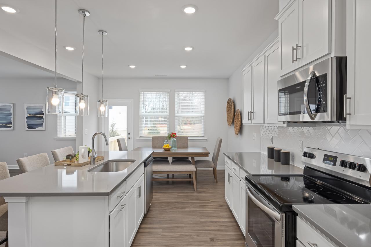 Spacious modern kitchen at Gregory Village in Lillington NC with white cabinets, quartz island, stainless appliances, and hardwood floors
