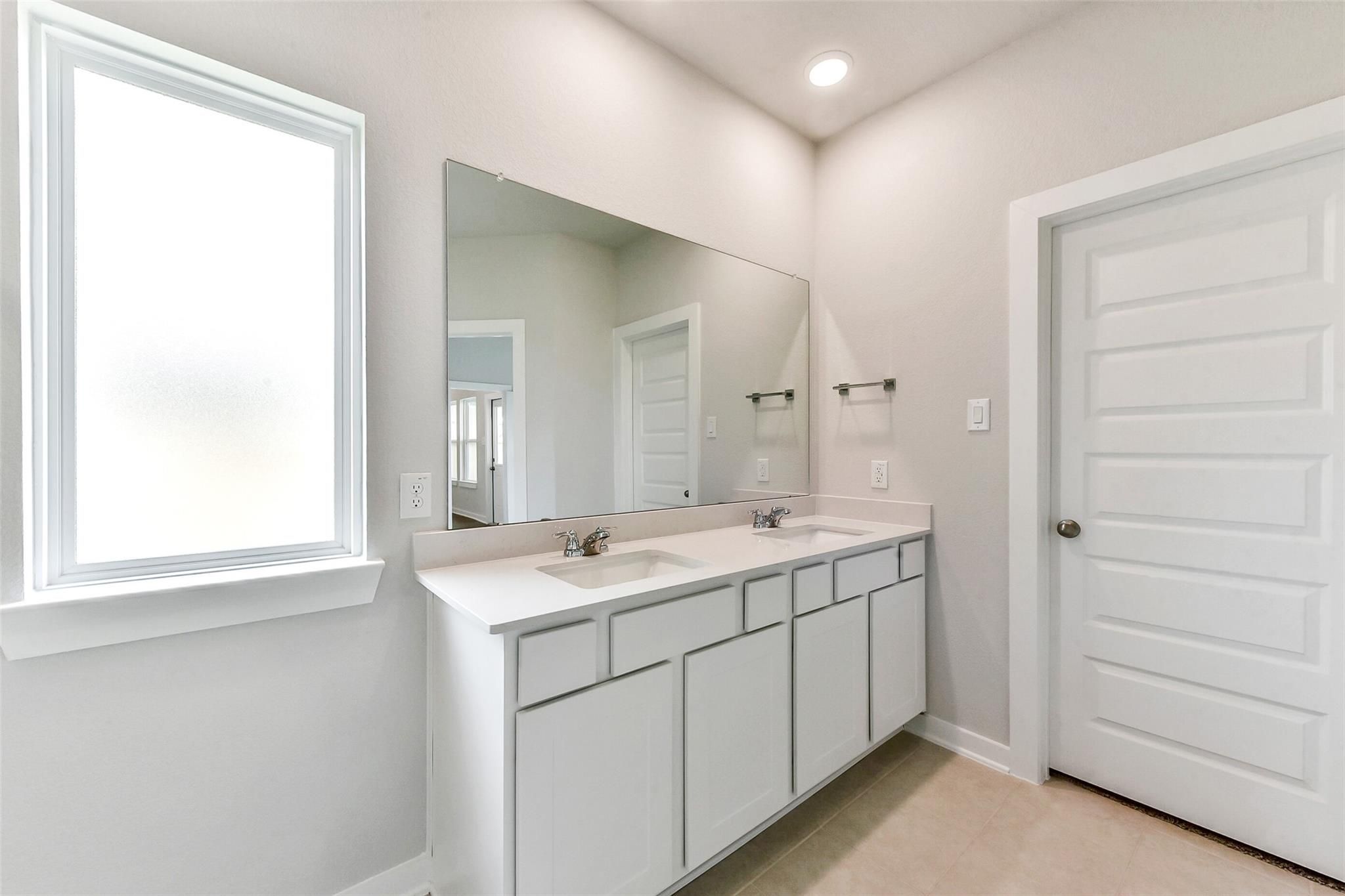 Modern master bathroom featuring double vanity sinks, large frameless mirror, and frosted window in Davidson Homes The Costa B, Dayton, Texas