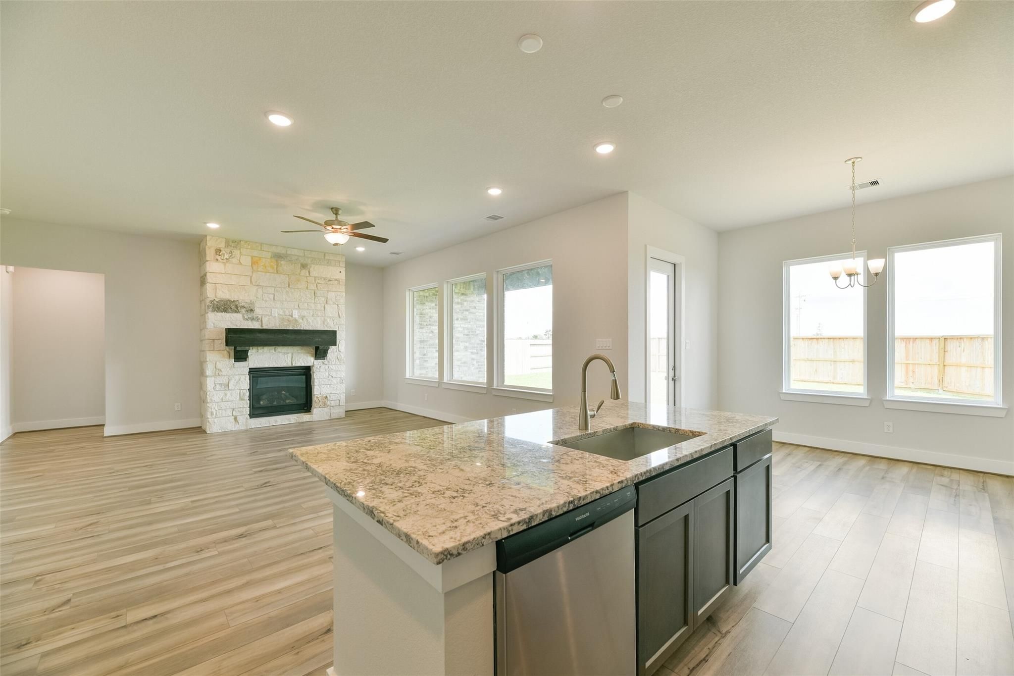 Open-concept living-kitchen with stone fireplace, granite island, stainless sink, and large windows in Davidson Homes The Edward A, Texas City