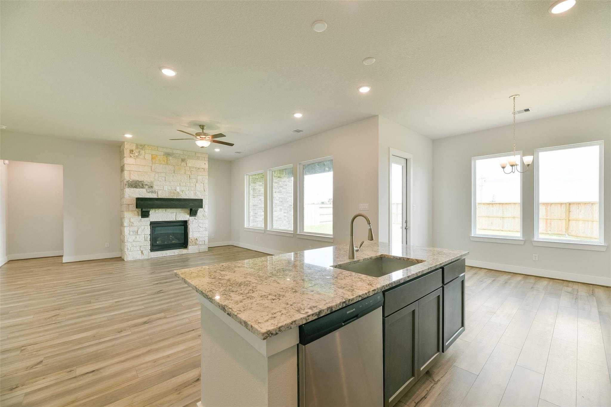 Open-concept living-kitchen with stone fireplace, granite island, stainless sink, and large windows in Davidson Homes The Edward A, Texas City