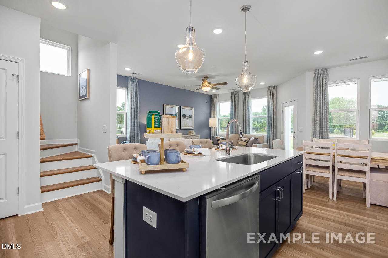 Open-concept kitchen with navy island, stainless appliances, hardwood floors, and dining nook in Davidson Homes The Graham, Fuquay-Varina