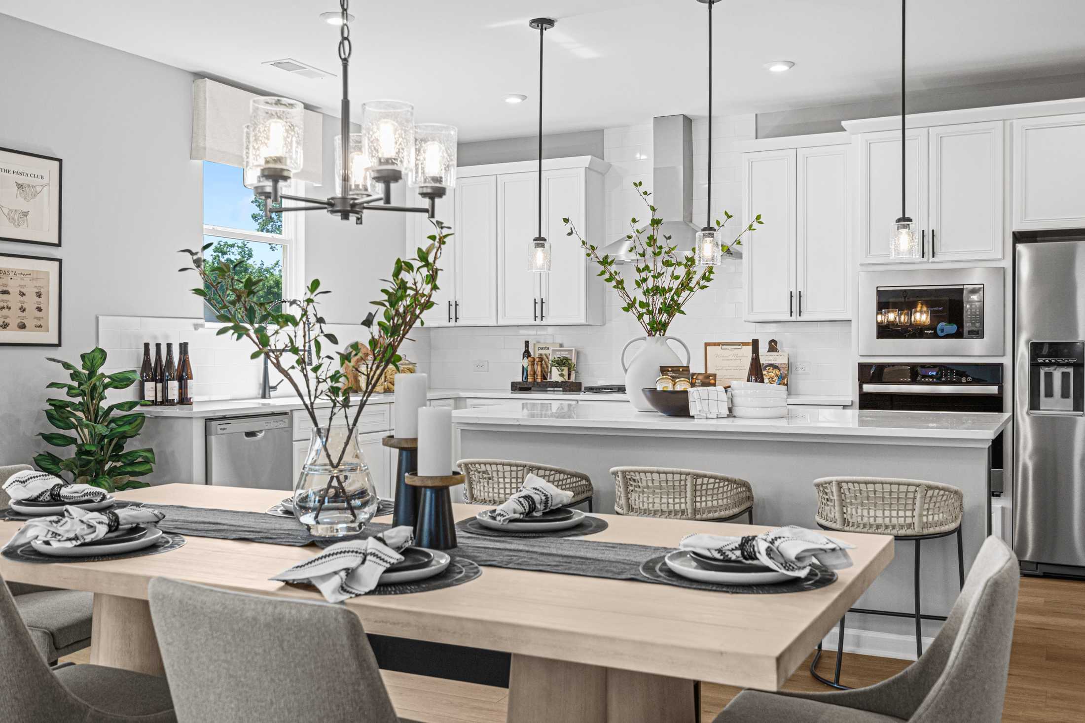 Spacious kitchen and dining in The Hickory A with white cabinets, stainless appliances, island bar, and modern pendant lights