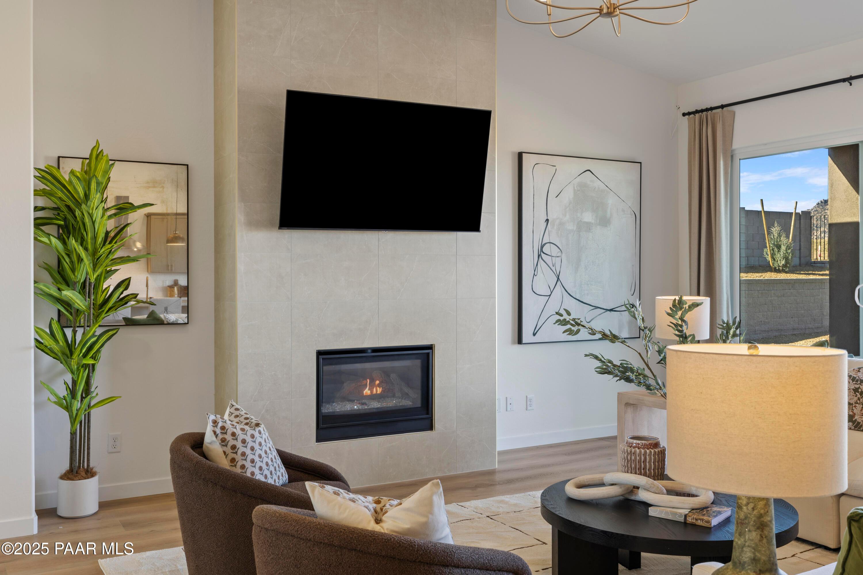 Cozy living room with stone gas fireplace, mounted TV, armchairs, and desert view in Davidson Homes The Blaze D, Prescott, Arizona