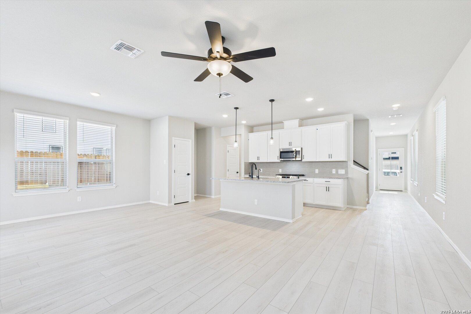 Bright open-concept kitchen and living area with white cabinets, island, ceiling fans, and light wood floors in The Charlotte A, San Antonio