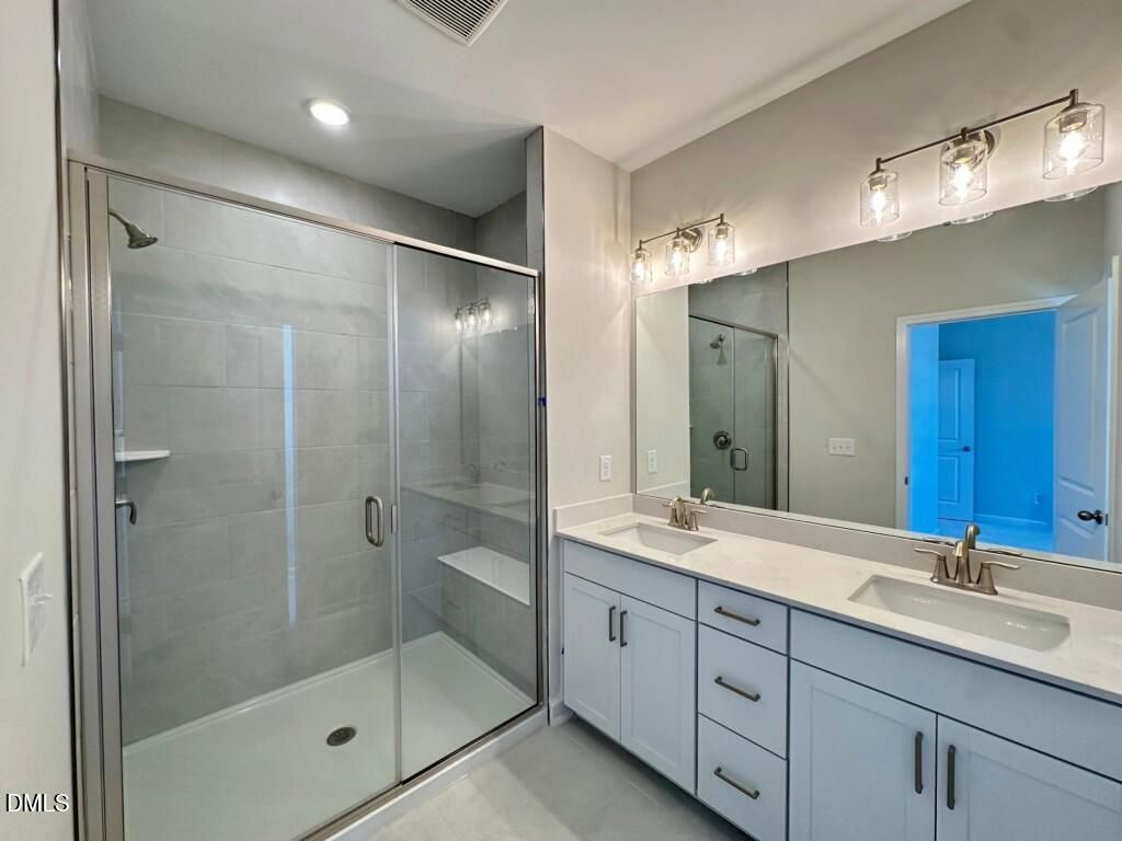 Modern master bathroom with frameless glass shower, double vanity sinks, and large mirror in Davidson Homes The Burke, Knightdale, NC