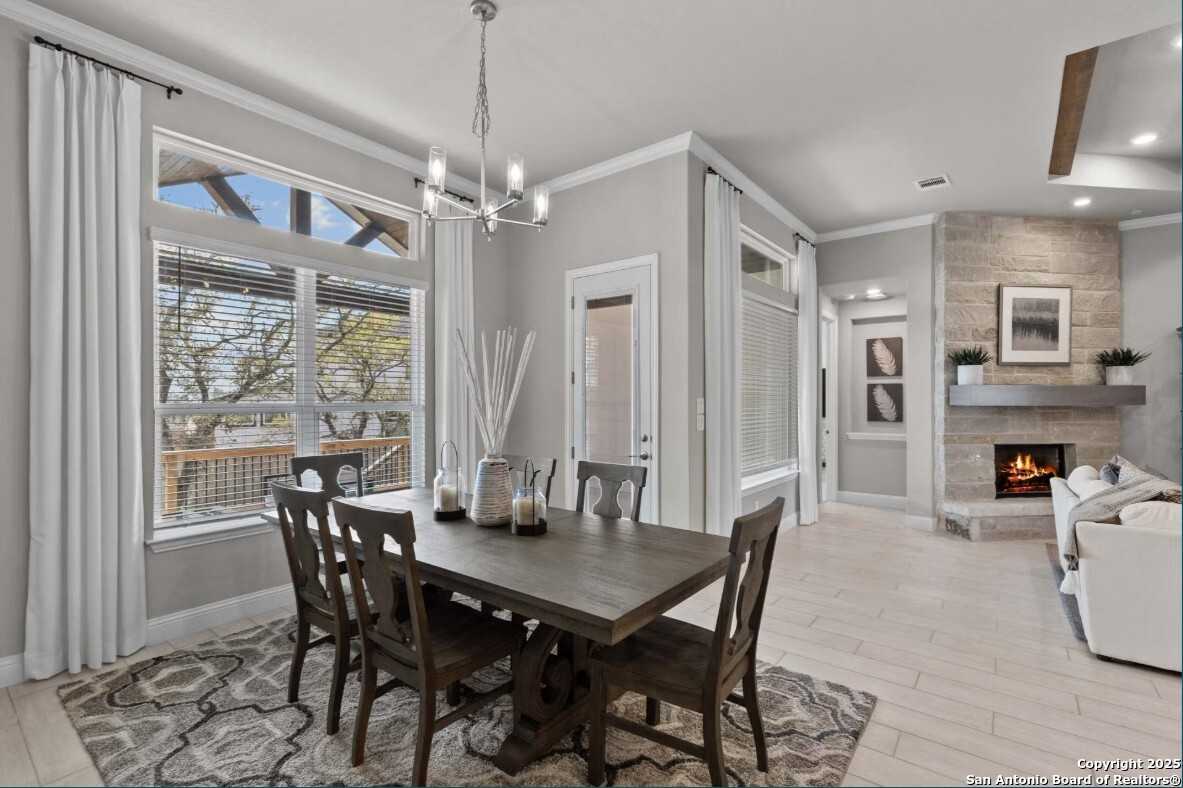 Elegant dining room with wooden table, chandelier, and large windows opening to living area with fireplace in Davidson Homes The Garner B, Ladera, San Antonio