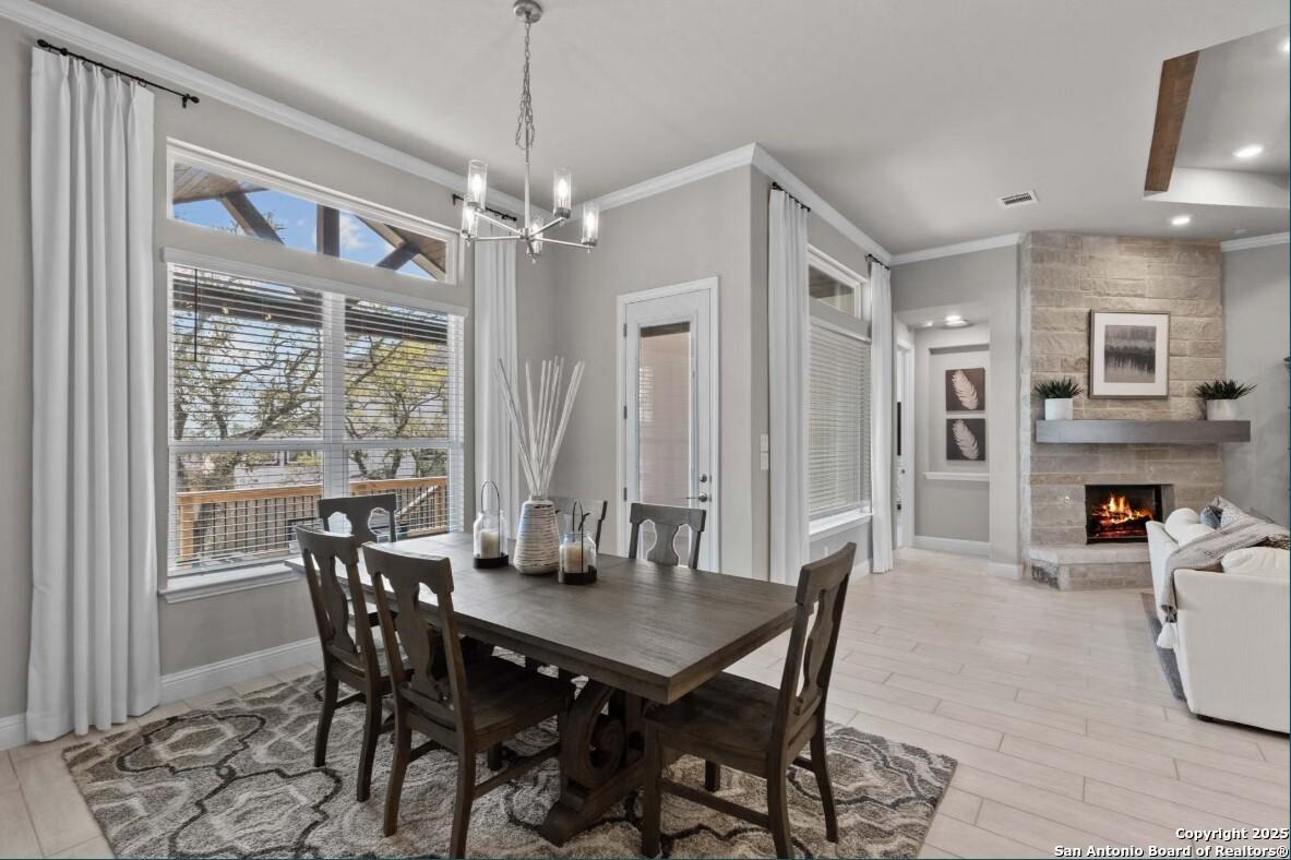 Elegant open-concept dining room with wooden farmhouse table, chandelier, and adjacent living space featuring stone fireplace in The Garner B, Ladera, San Antonio