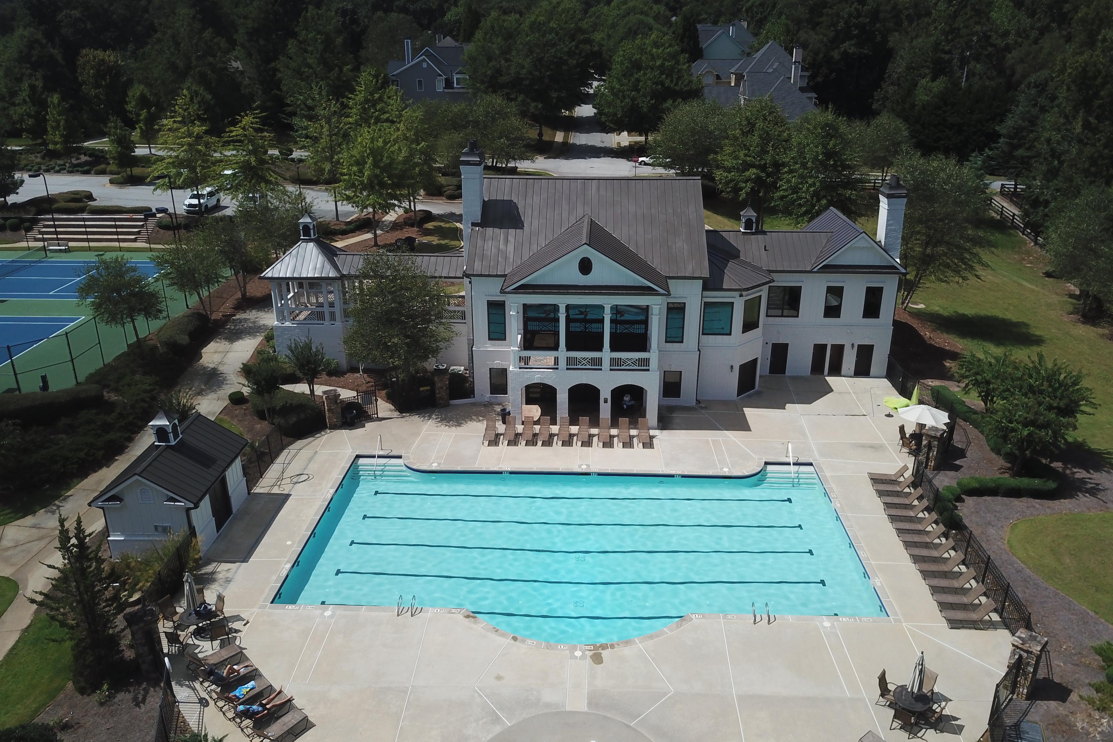 Aerial view of resort-style swimming pool and clubhouse at Riverwood in Dallas Georgia with tennis courts lounge chairs and surrounding greenery