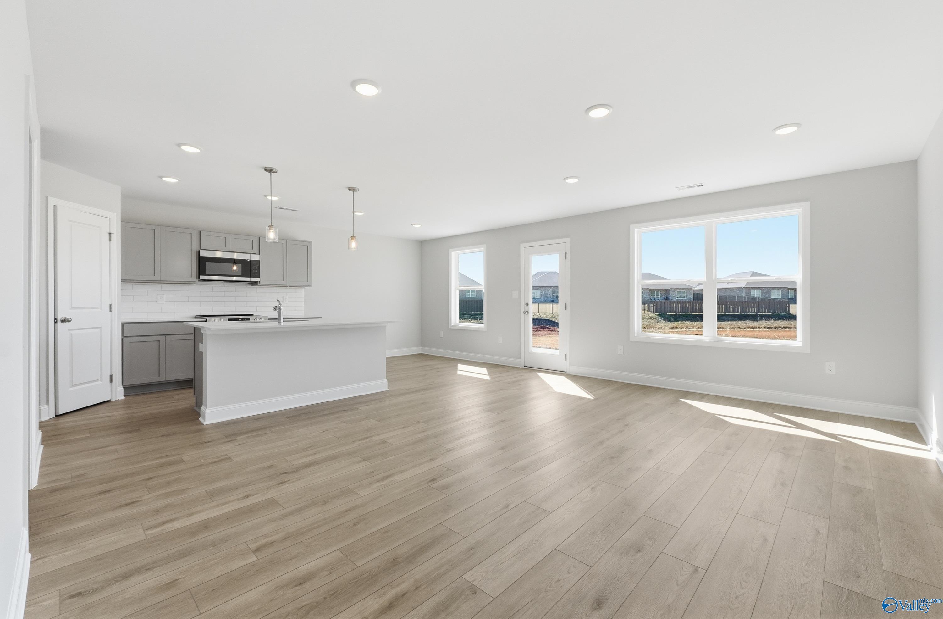 Open-concept kitchen with gray cabinets, large island sink, stainless appliances, and hardwood floors in Davidson Homes The Butler, New Market, Alabama