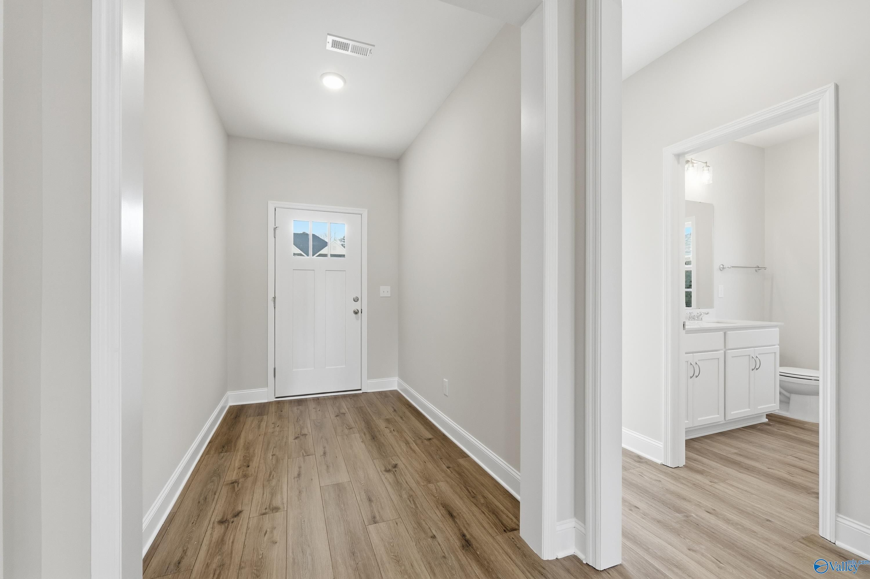 Bright entryway hallway with wood flooring, front door, and adjacent powder room in The Everett 4-bedroom home, Harvest, Alabama