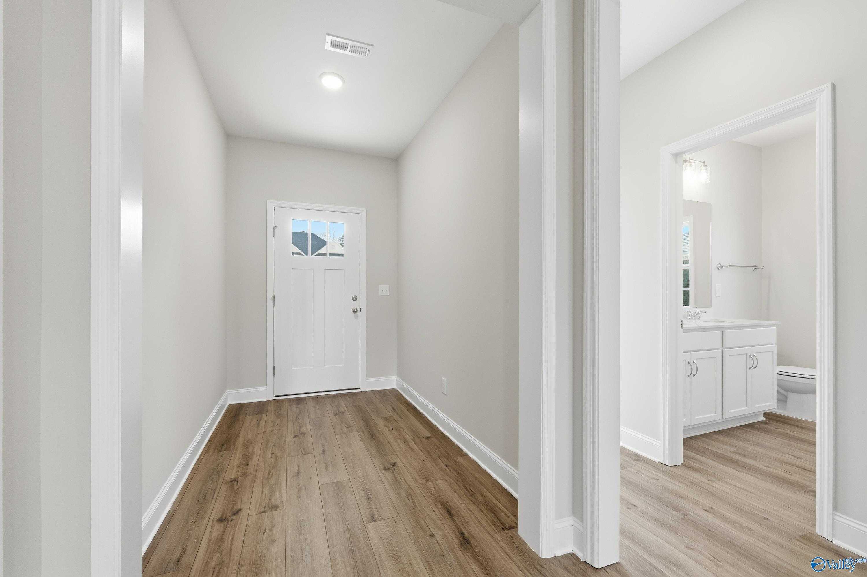 Bright entryway hallway with wood flooring, front door, and adjacent powder room in The Everett 4-bedroom home, Harvest, Alabama