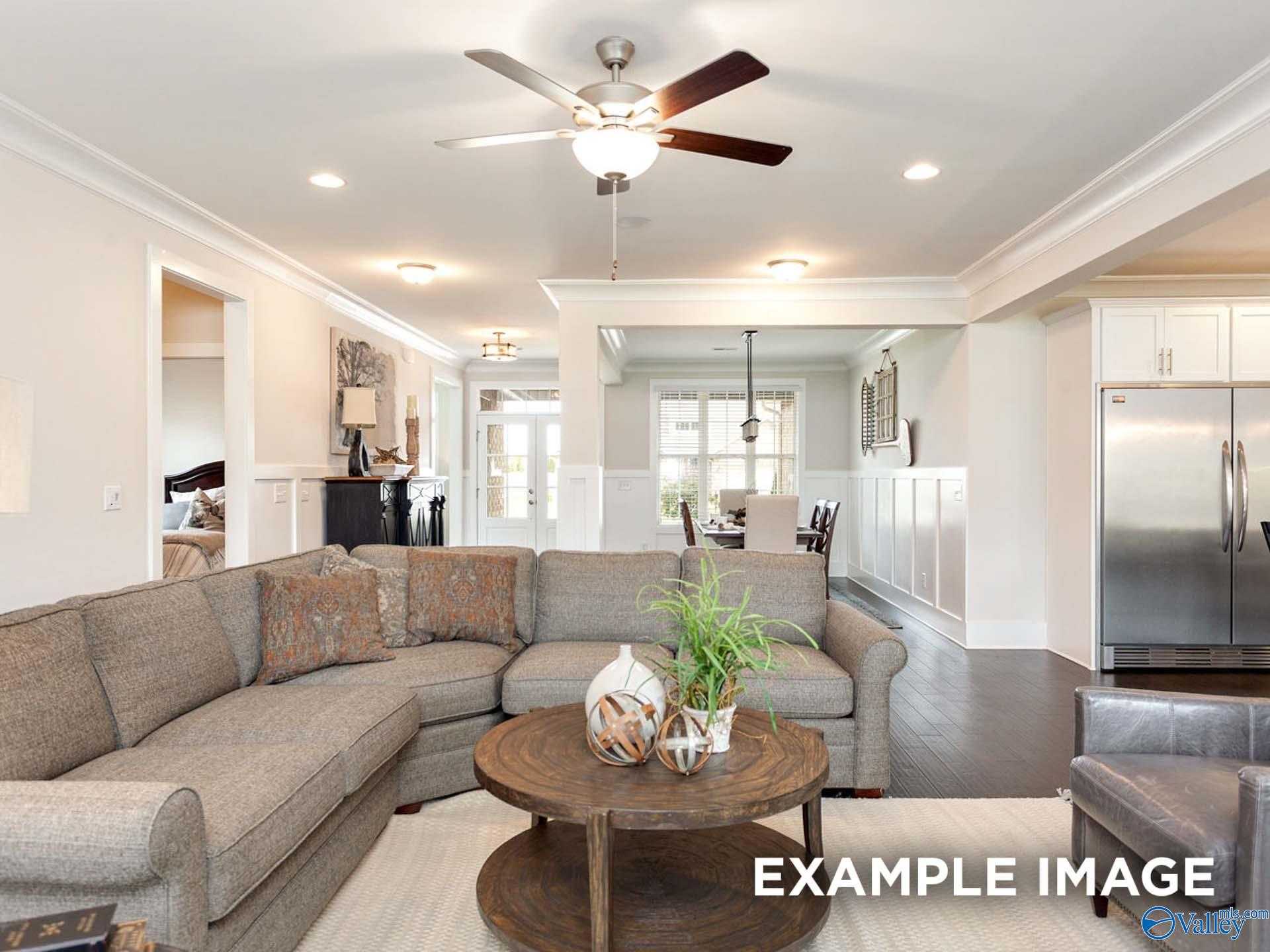 Open-concept living room with gray L-shaped sofa, wood coffee table, ceiling fan, and kitchen view in Davidson Homes The Finleigh, Meridianville, Alabama