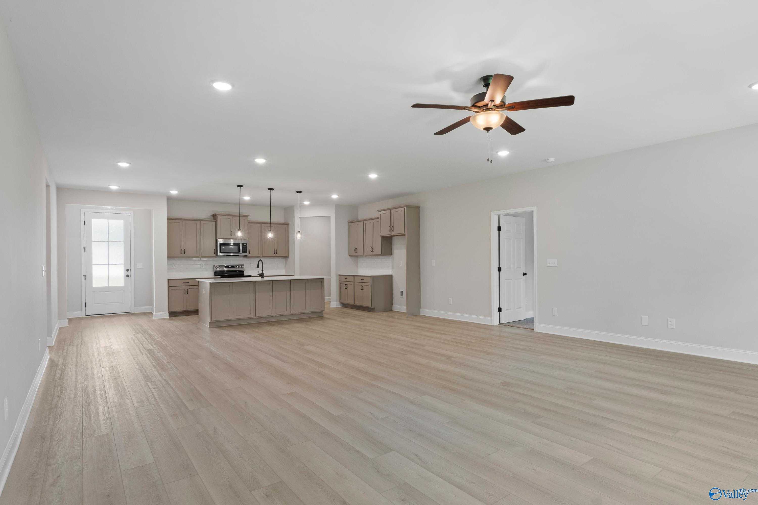 Spacious open-concept kitchen-living area with large island, light wood cabinets, hardwood floors, ceiling fan in Davidson Homes The Kirkland, Harvest AL
