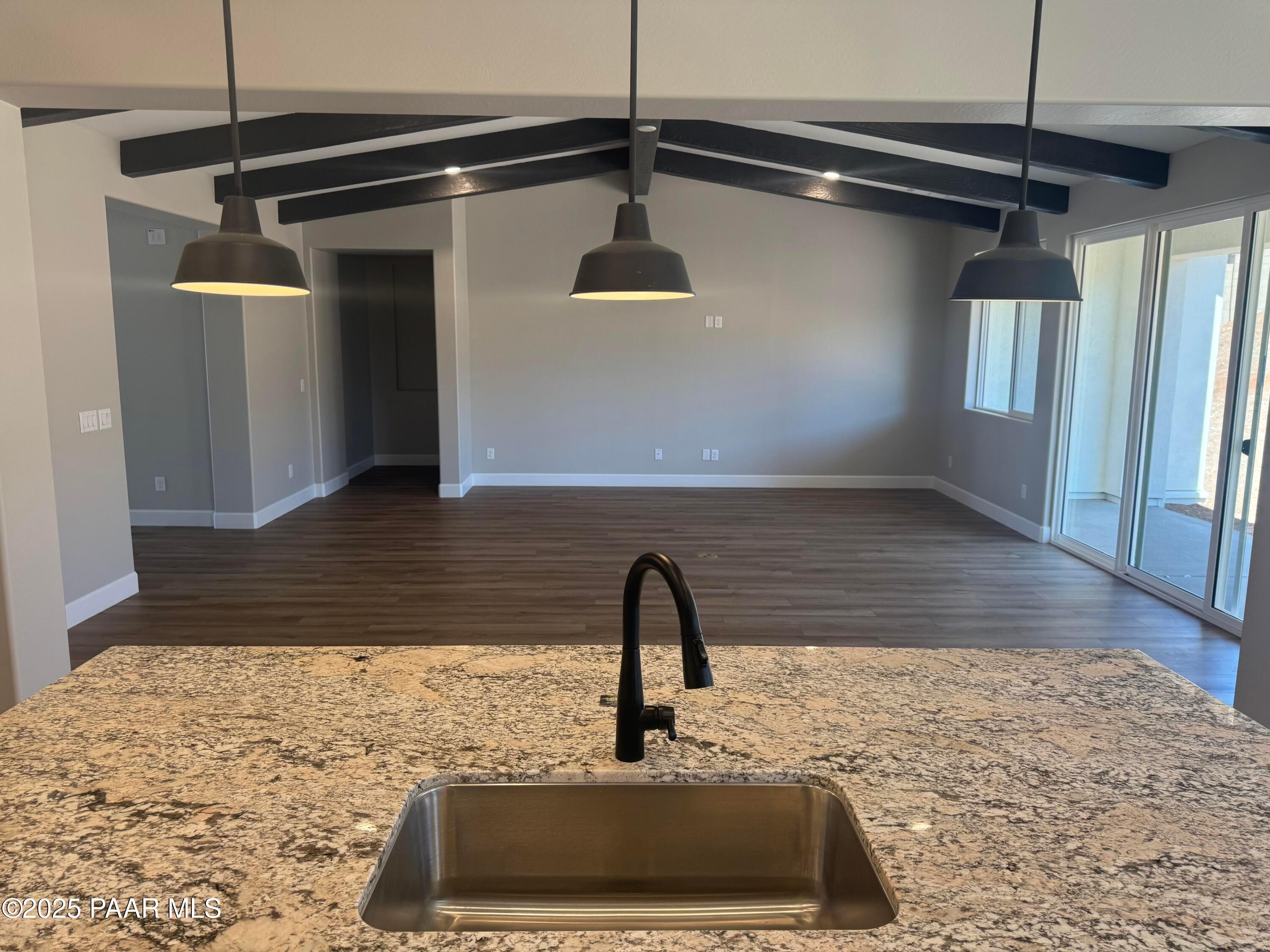Modern kitchen island with granite countertop, stainless sink, and black faucet under pendant lights and wooden beams in open living space, The Summit B, Prescott Valley, AZ