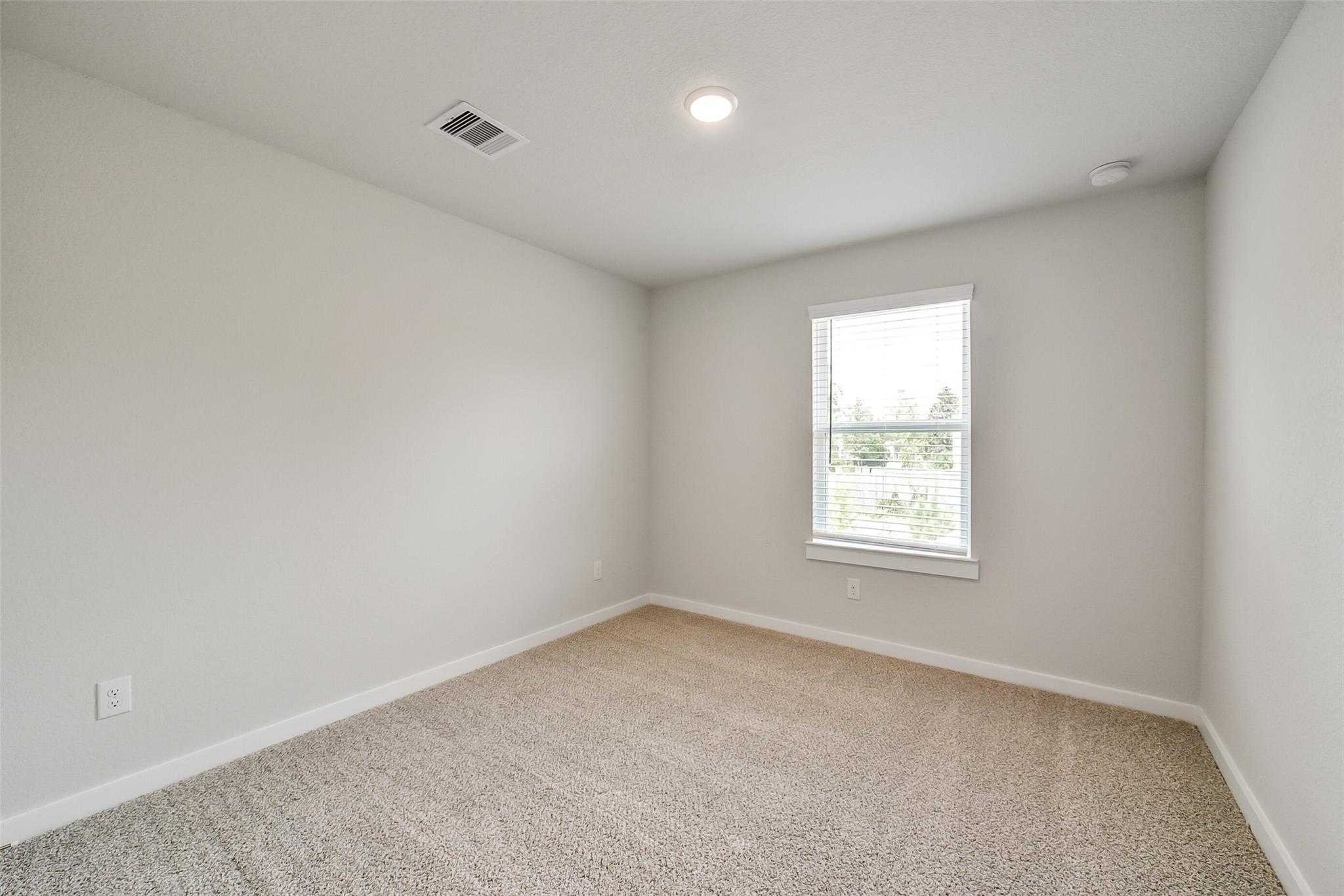 Bright empty secondary bedroom with light gray walls, beige carpet, and window blinds in Davidson Homes The Trinity F, Magnolia, Texas