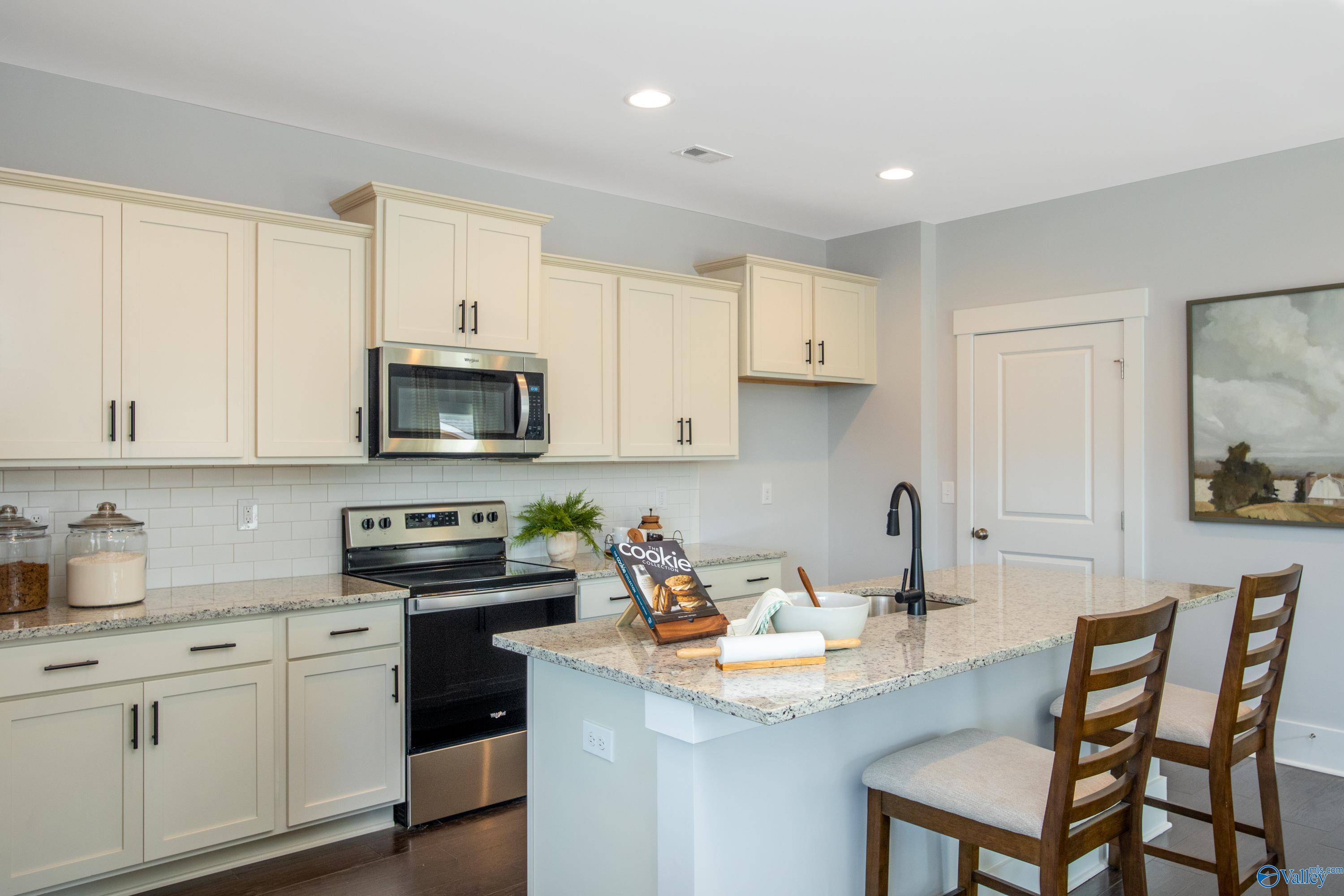 Modern kitchen featuring white shaker cabinets, stainless steel appliances, granite island, and bar stools in Davidson Homes The Covington C, Decatur, Alabama
