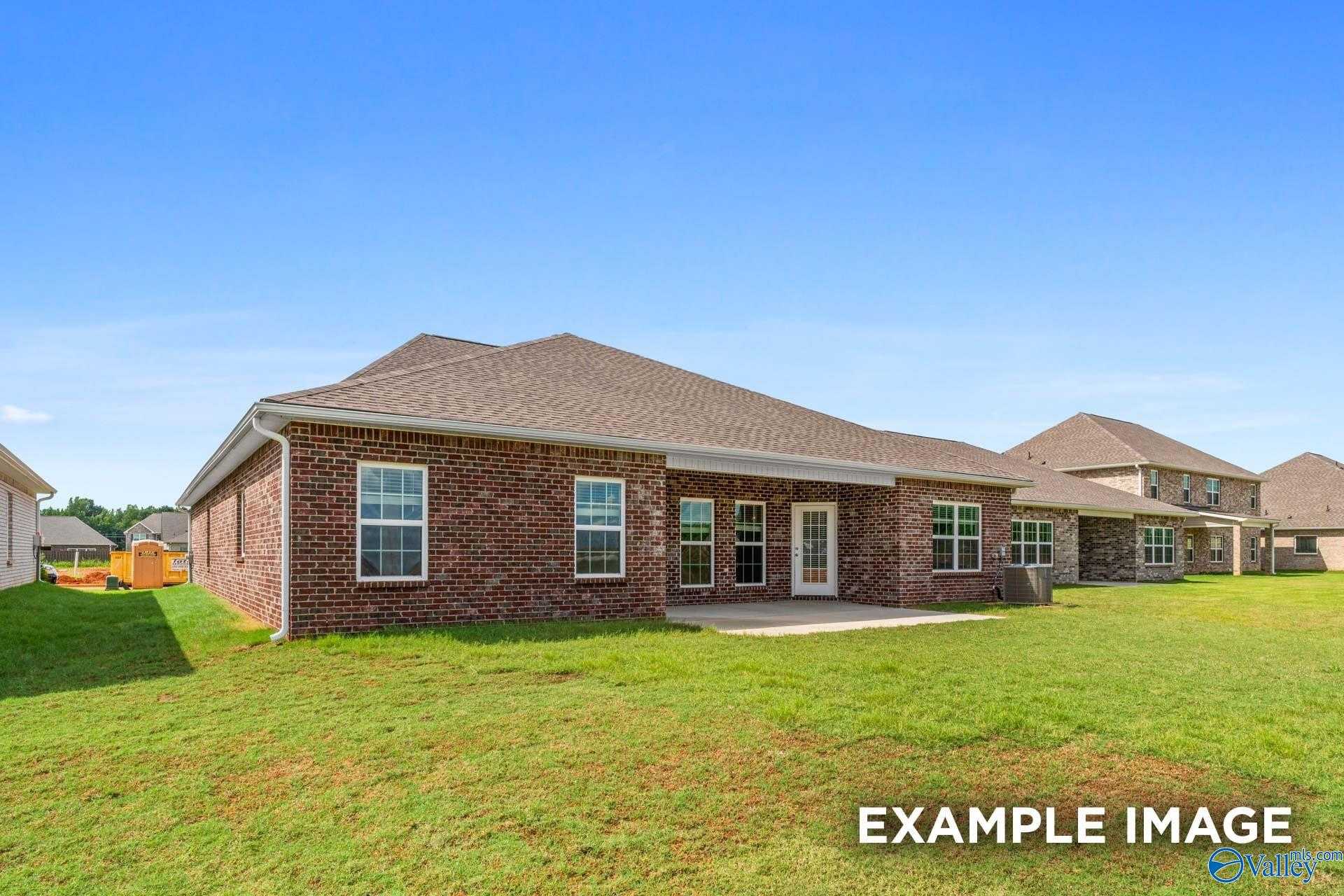 Rear view of single-story brick home with covered patio, large windows, and lush green lawn in River Road Estates, Decatur, Alabama