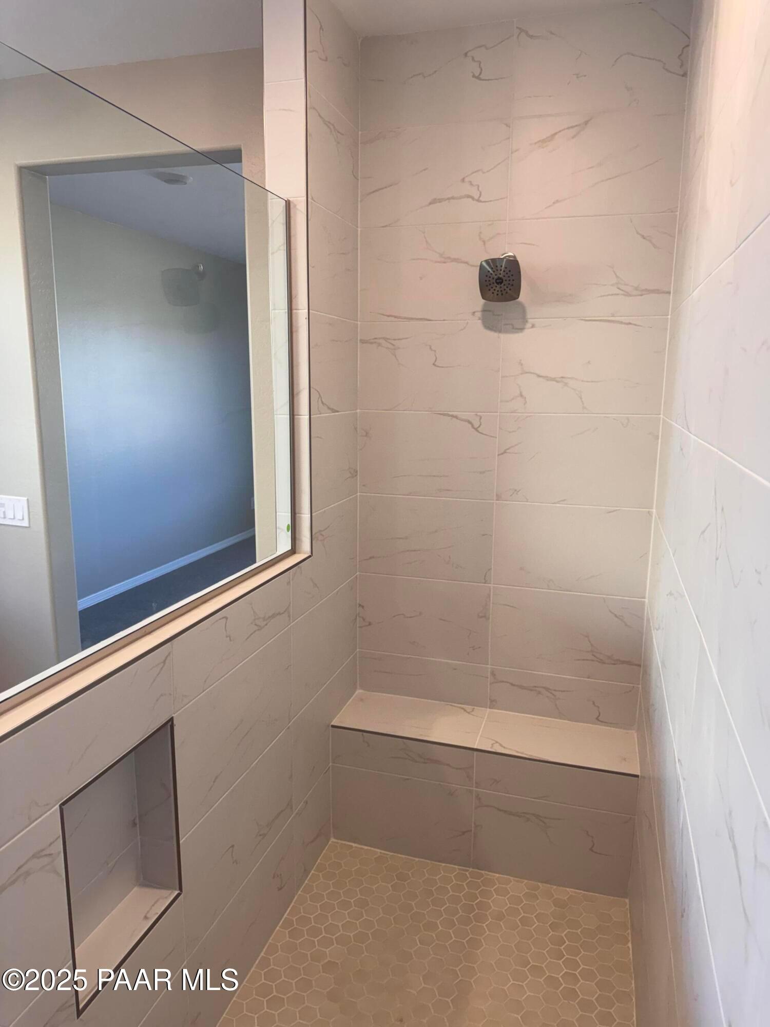 Elegant walk-in shower with white veined tiles, built-in bench, niche, and rain showerhead in Davidson Homes The Sunrise II A, Prescott, AZ