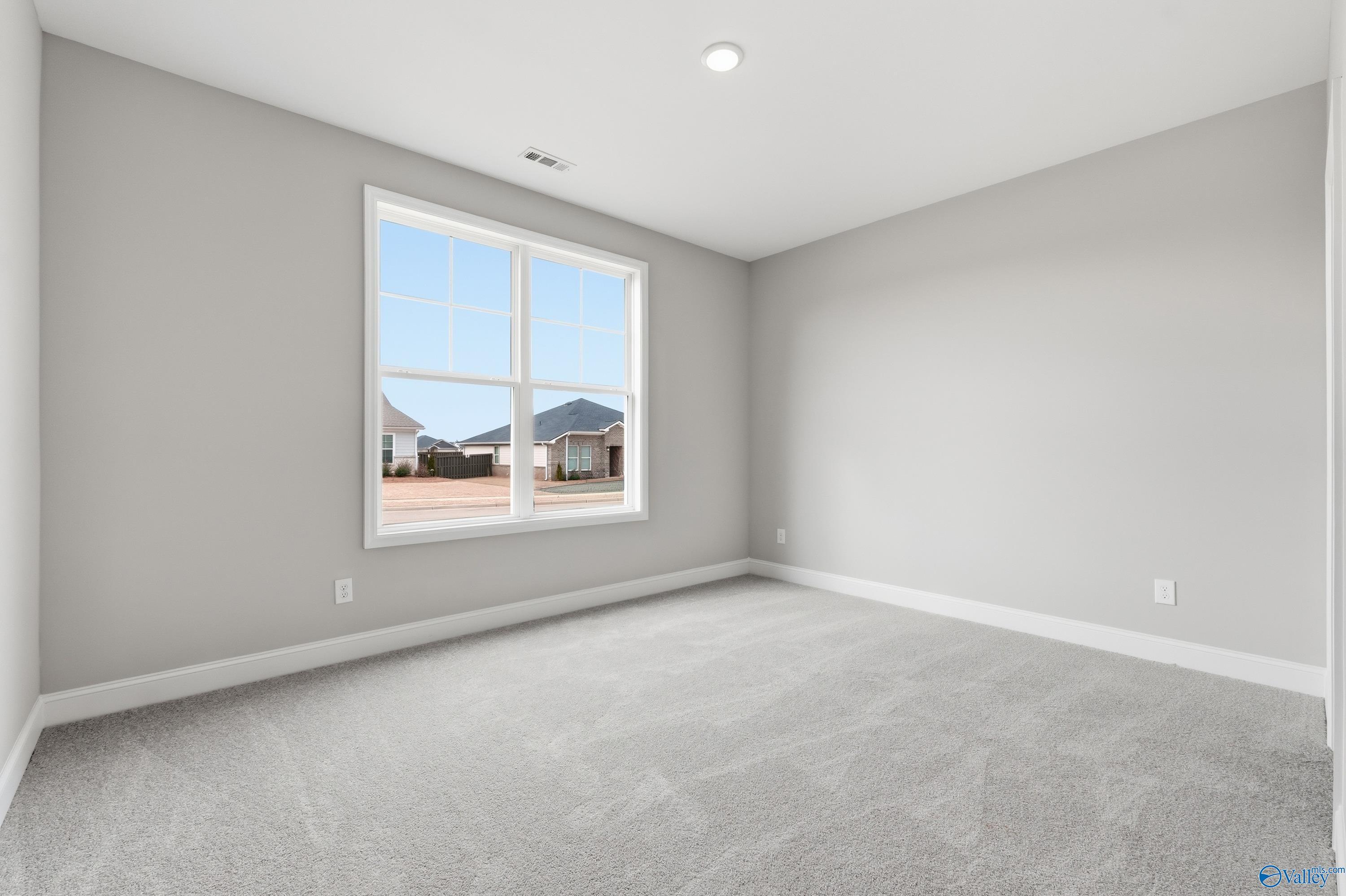 Empty bedroom with light gray walls, gray carpet floor, and large window overlooking neighborhood houses in Davidson Homes The Rockford C, Athens, Alabama