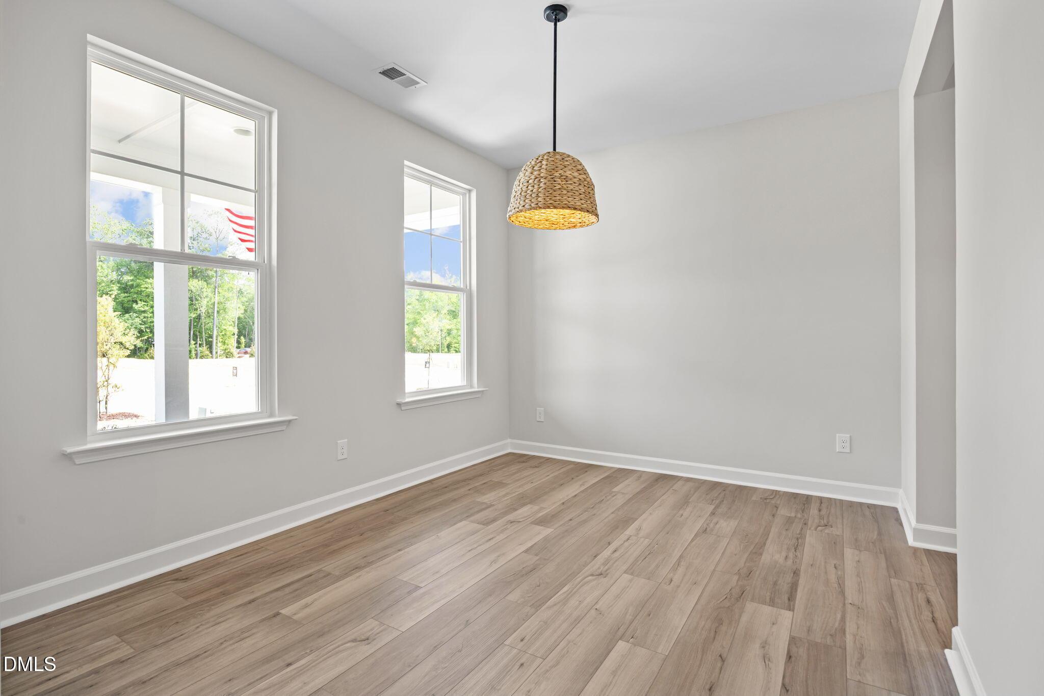 Bright bedroom with large windows overlooking greenery, woven pendant light, and light hardwood floors in The Willow D, Wendell, NC