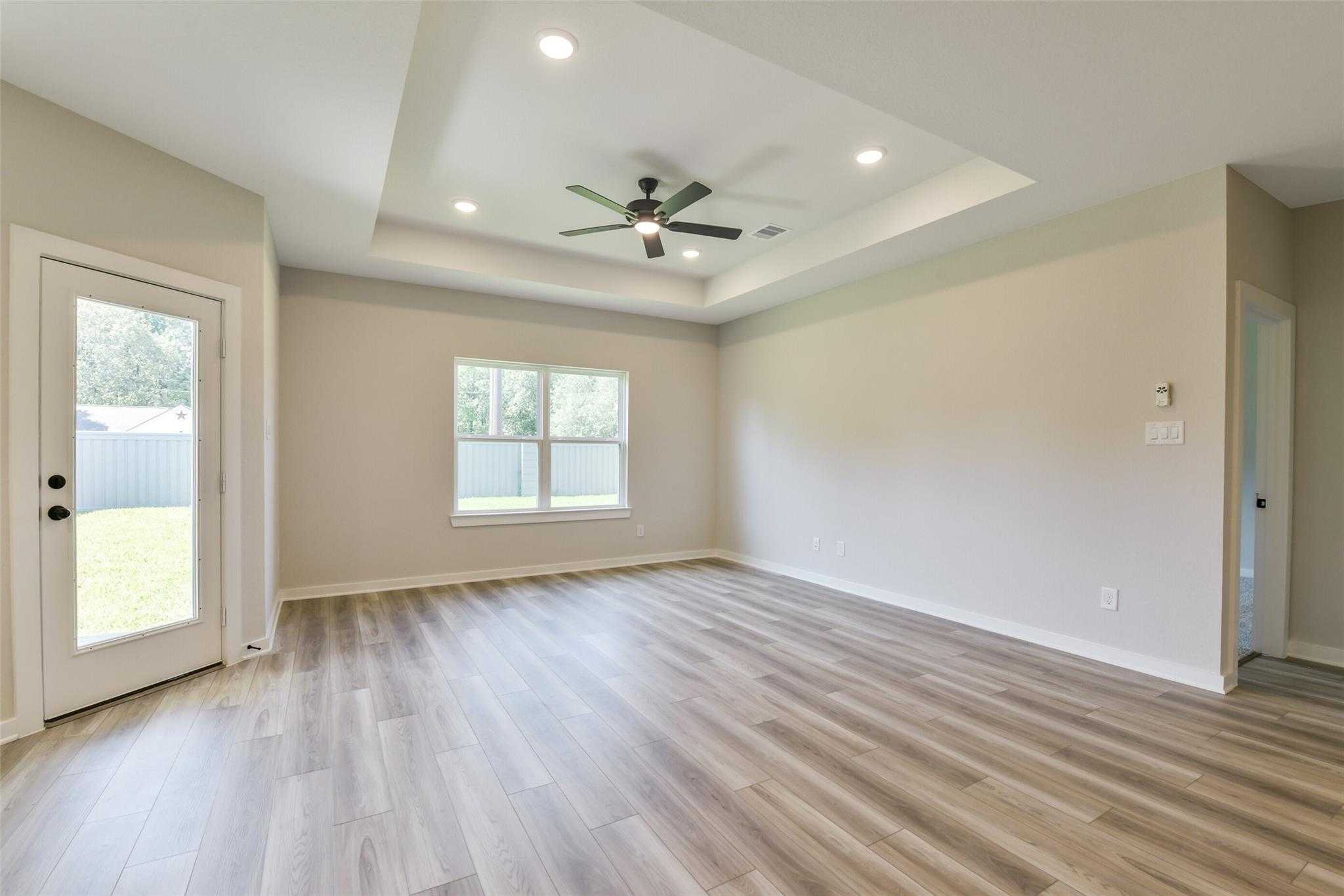 Spacious living room with tray ceiling, ceiling fan, French doors to backyard, and luxury vinyl plank flooring in Davidson Homes The Daphne H, Crosby, Texas