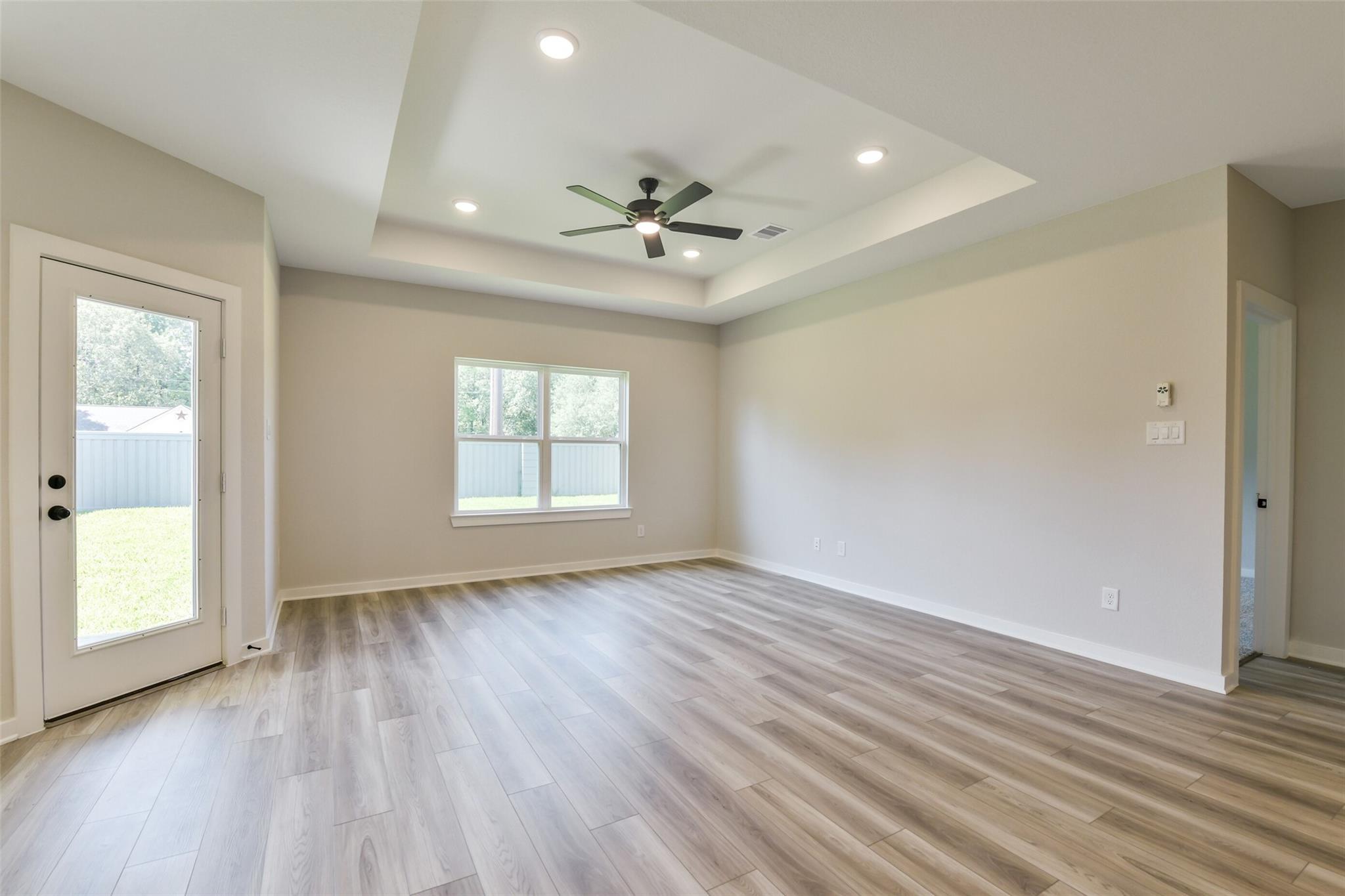 Spacious living room with tray ceiling, ceiling fan, French doors to backyard, and luxury vinyl plank flooring in Davidson Homes The Daphne H, Crosby, Texas