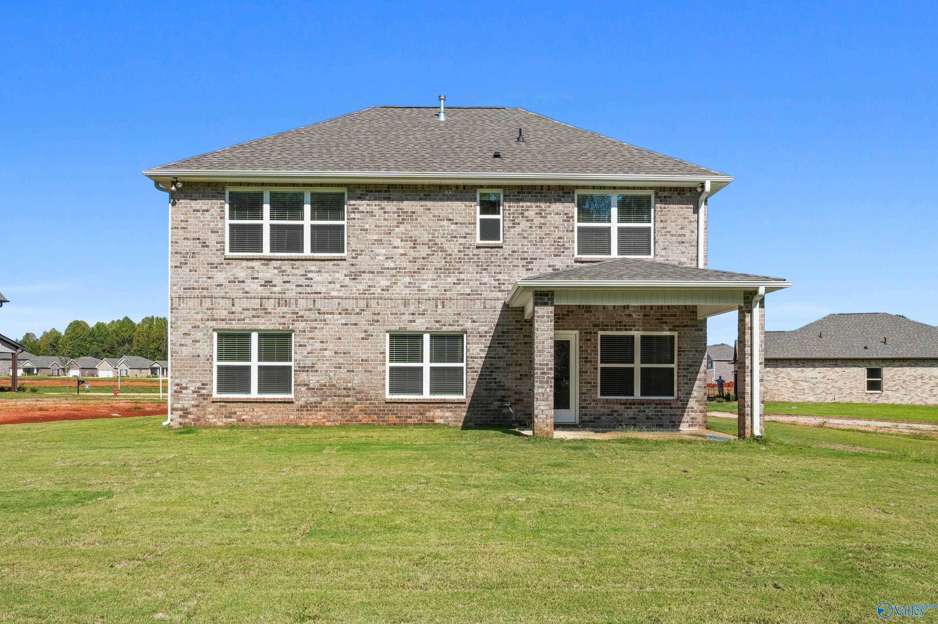 Rear view of two-story brick Davidson Homes Shelby A with covered patio, large windows, and lush green lawn in Ricketts Farm, Athens, Alabama